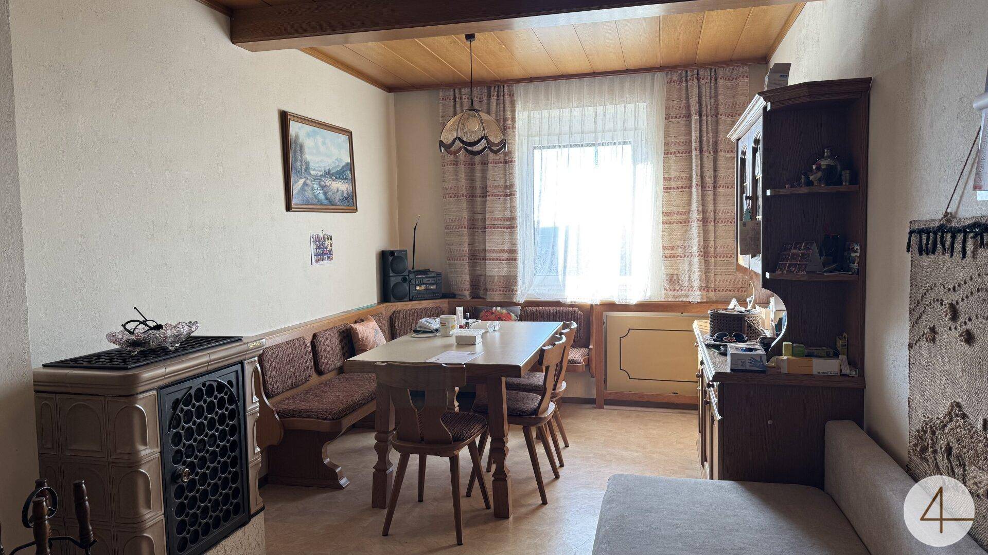 Gemütlicher Wohn-Essbereich mit traditionellem Kachelofen, Holztisch und Sitzbank.