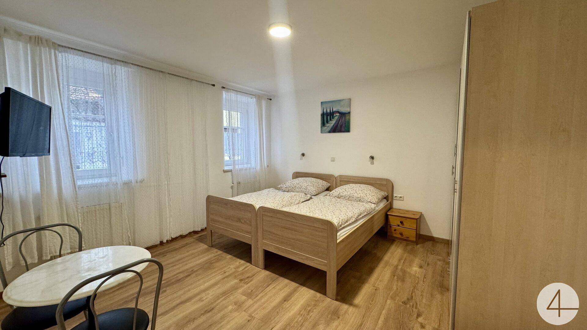 Helles Schlafzimmer mit zwei Einzelbetten, kleinem Tisch und Fernseher, ausgestattet mit Laminatboden.