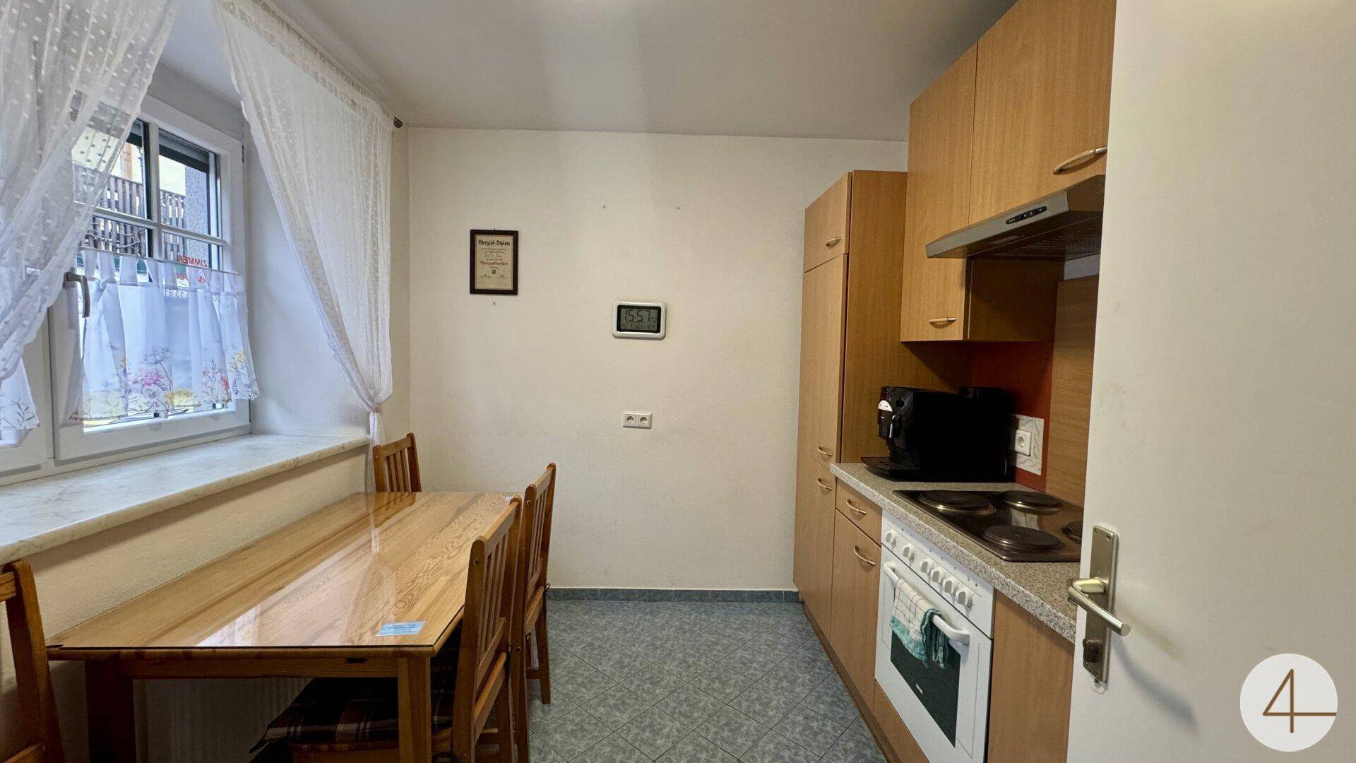 Funktionale Küche mit Holzschränken, Herd, Backofen und Esstisch am Fenster in gutem Zustand.