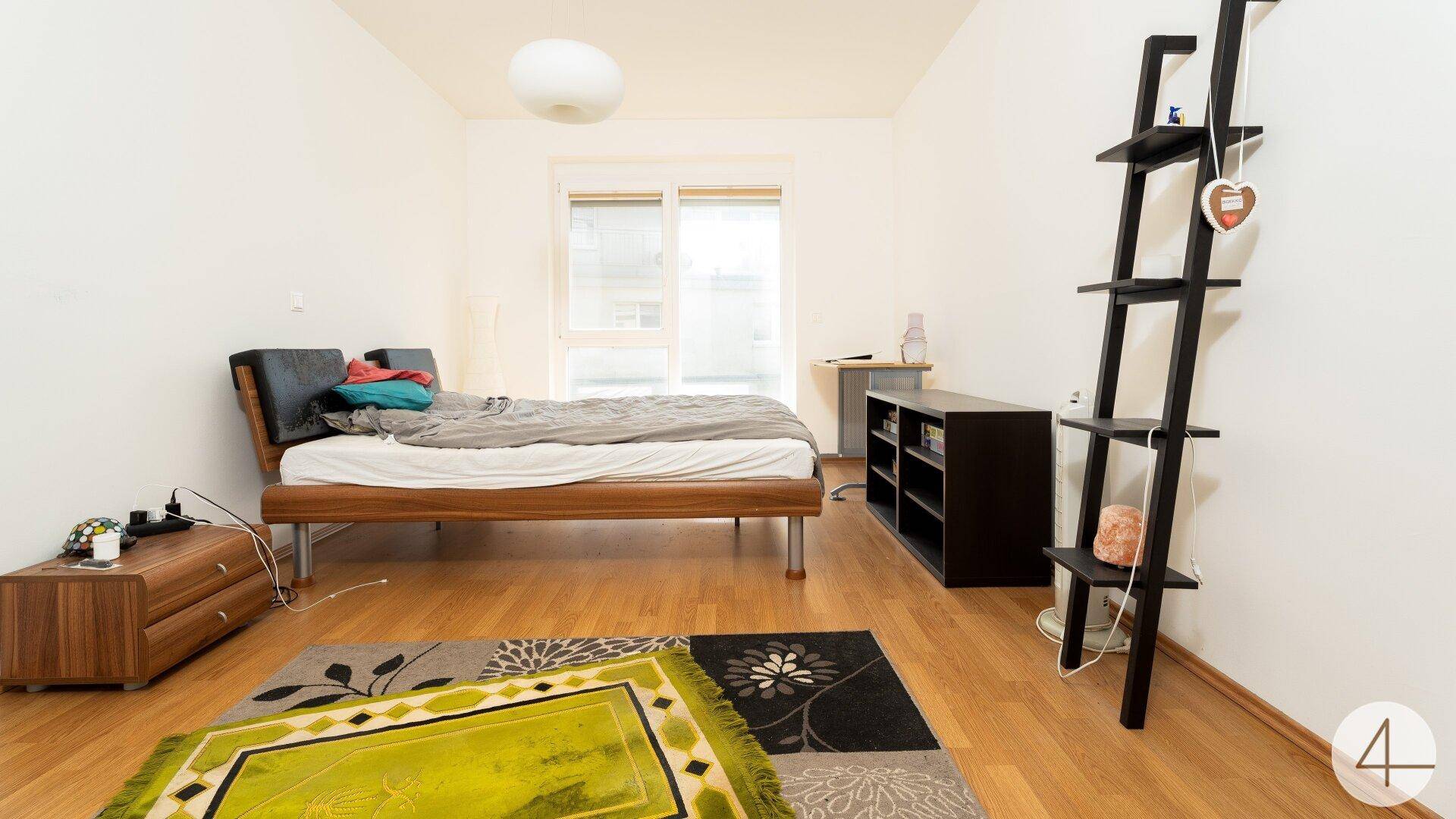 Helles Schlafzimmer mit Parkettboden und großem Fenster, bietet eine ruhige Rückzugsmöglichkeit.