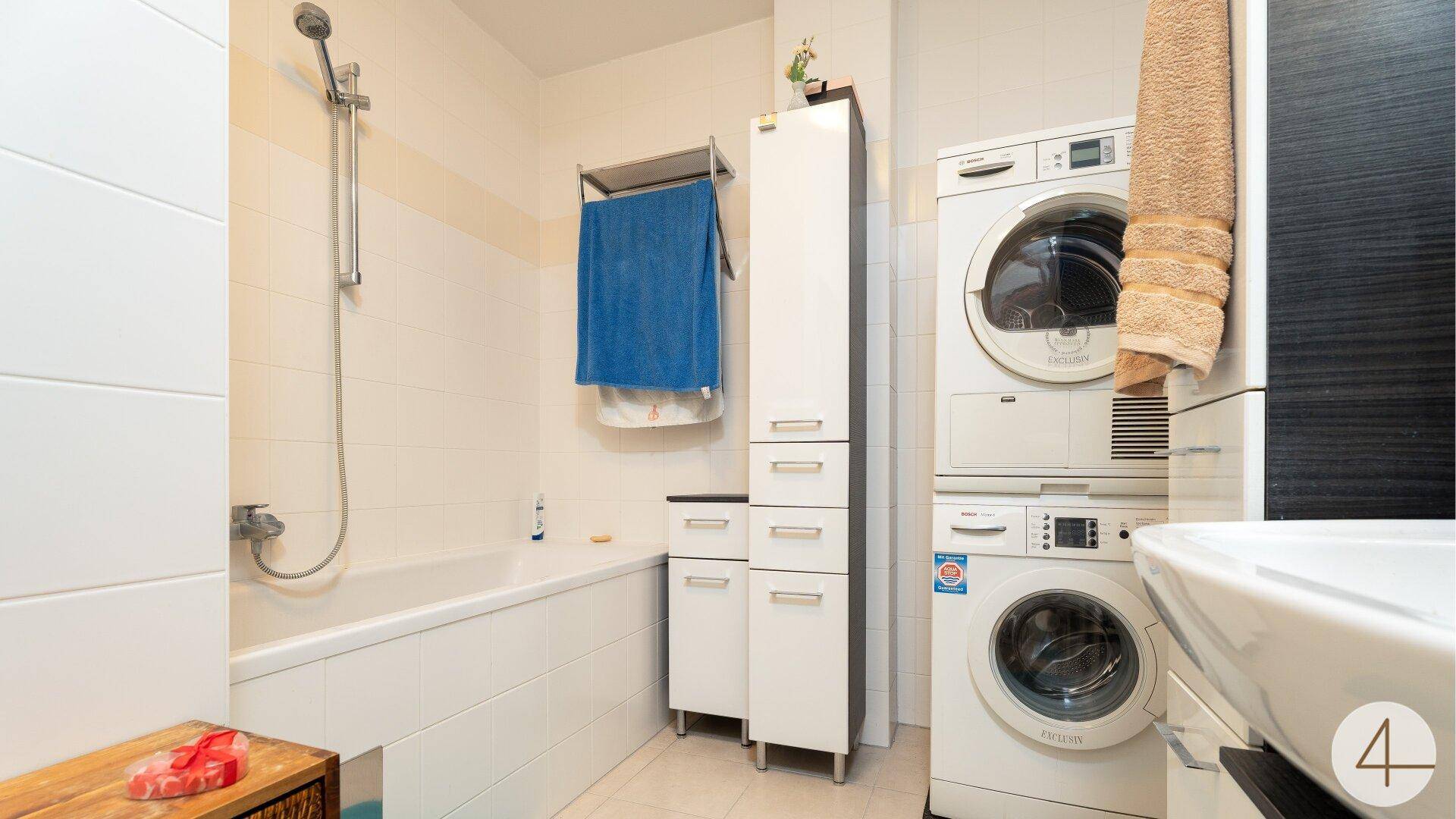 Badezimmer mit Badewanne, integrierter Dusche und praktischer Waschmaschine sowie Trockner.