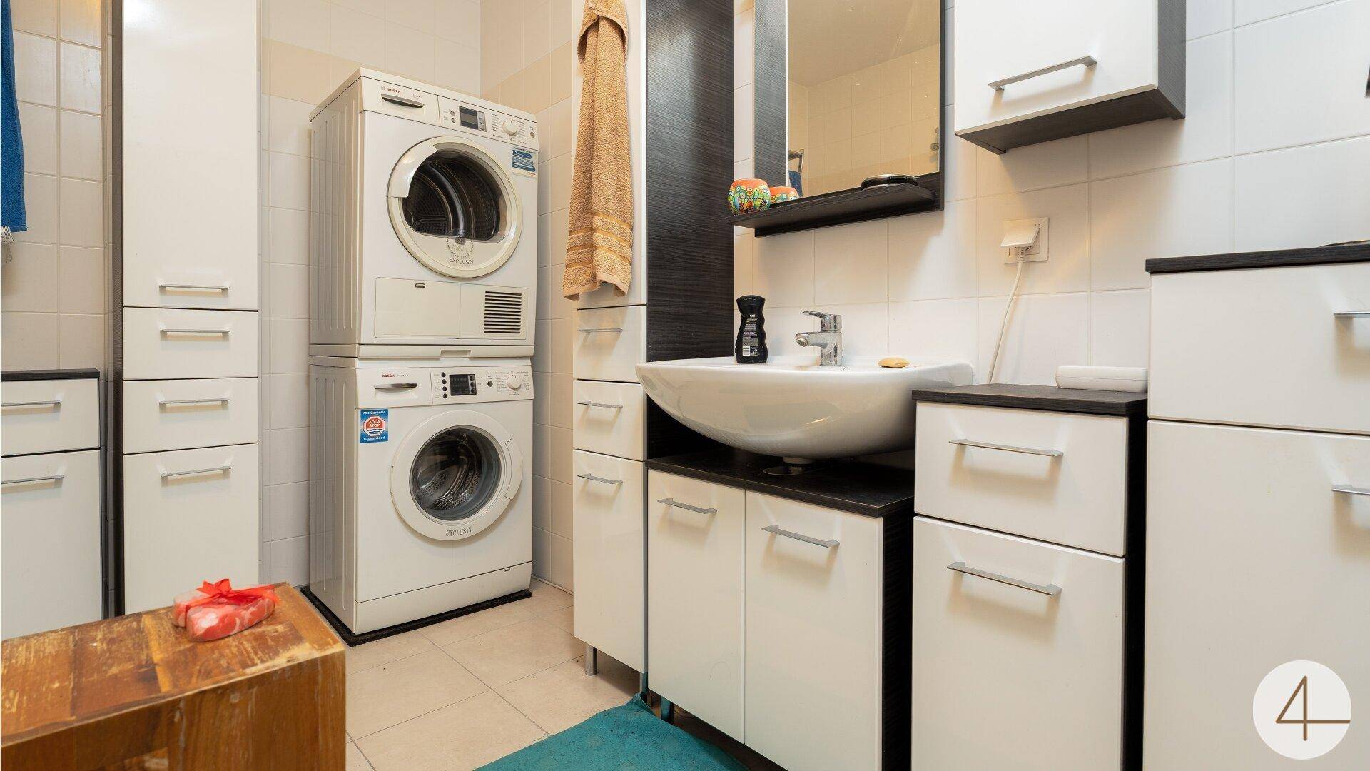 Modernes Badezimmer mit Waschbecken, Spiegelschrank und integrierter Waschmaschine und Trockner.