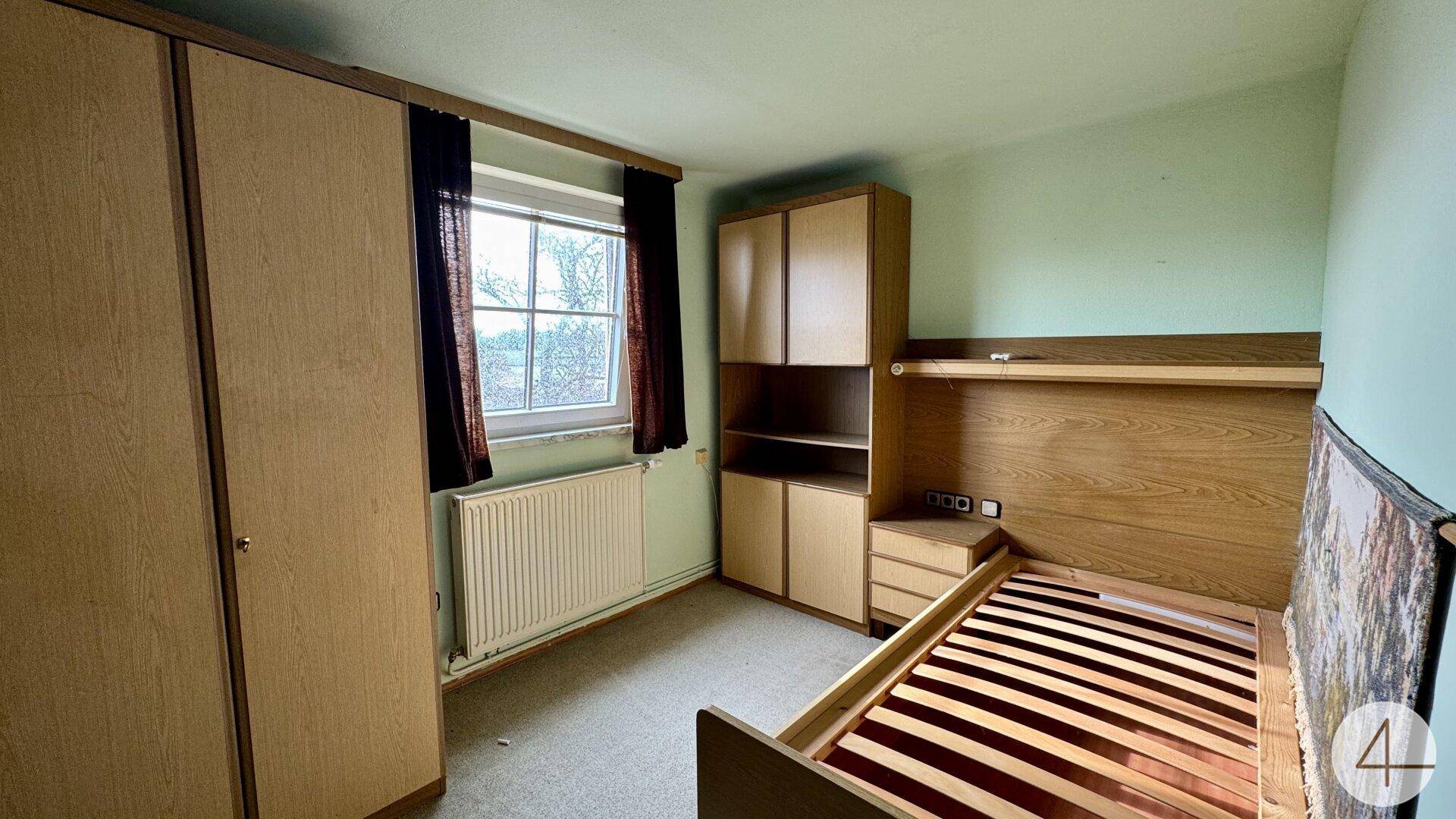 Schlafzimmer mit grünen Wänden, einfachen Holzmöbeln und einem Fenster mit Blick nach draußen.