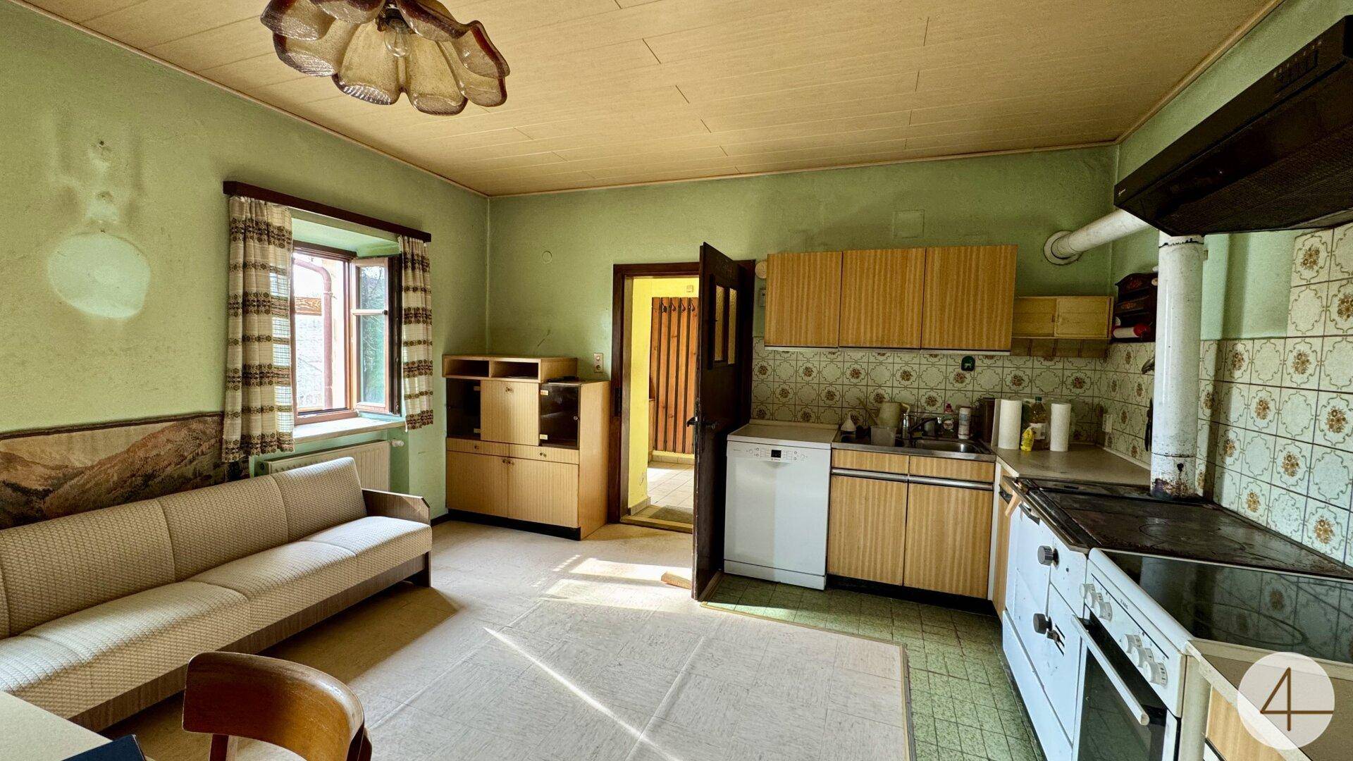 Rustikale Küche mit grünen Wänden, älteren Holzschränken und einem Sofa in renovierungsbedürftigem Zustand.