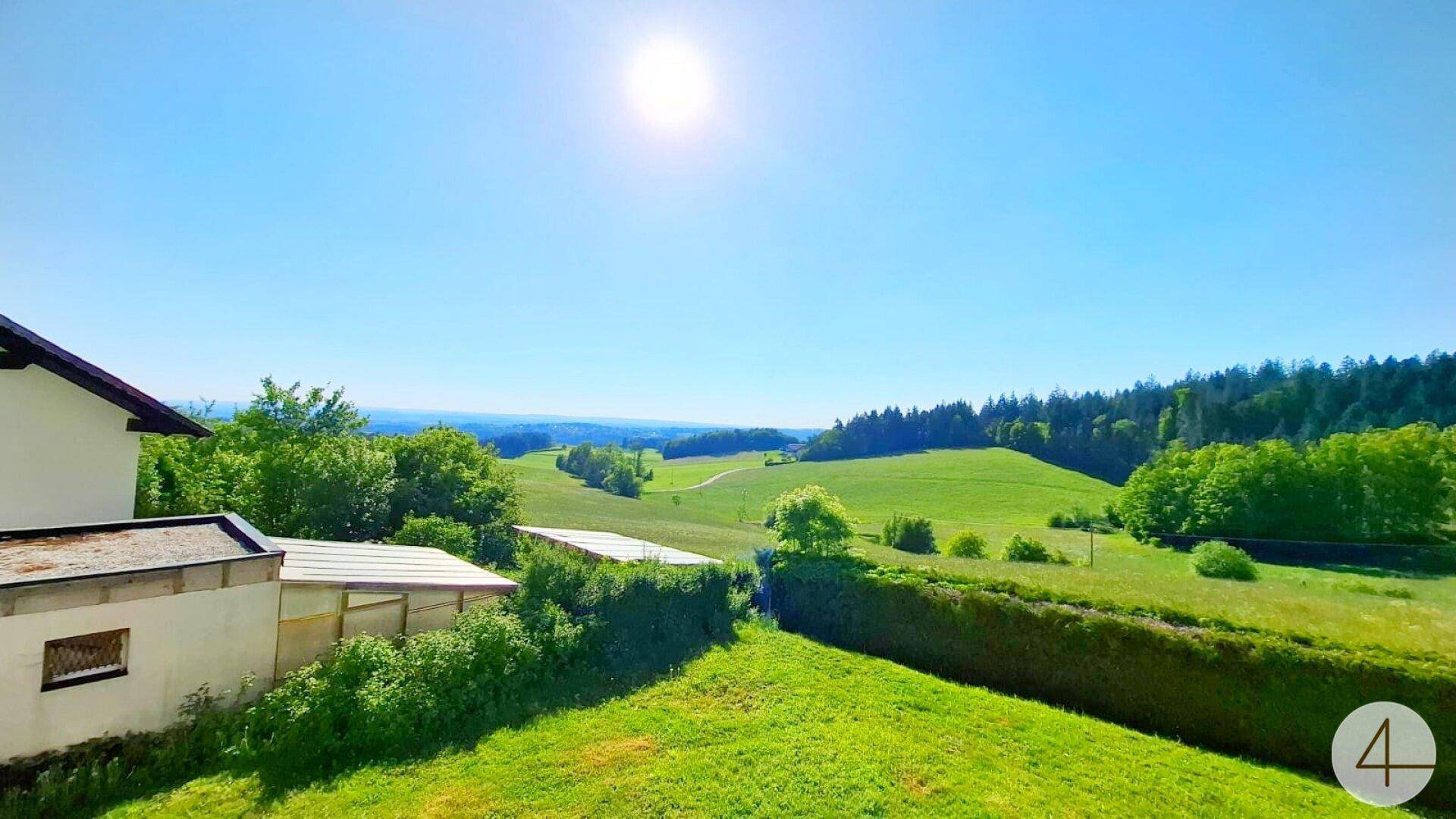 Weitläufiger Blick über grüne Hügel und Wälder unter strahlend blauem Himmel.