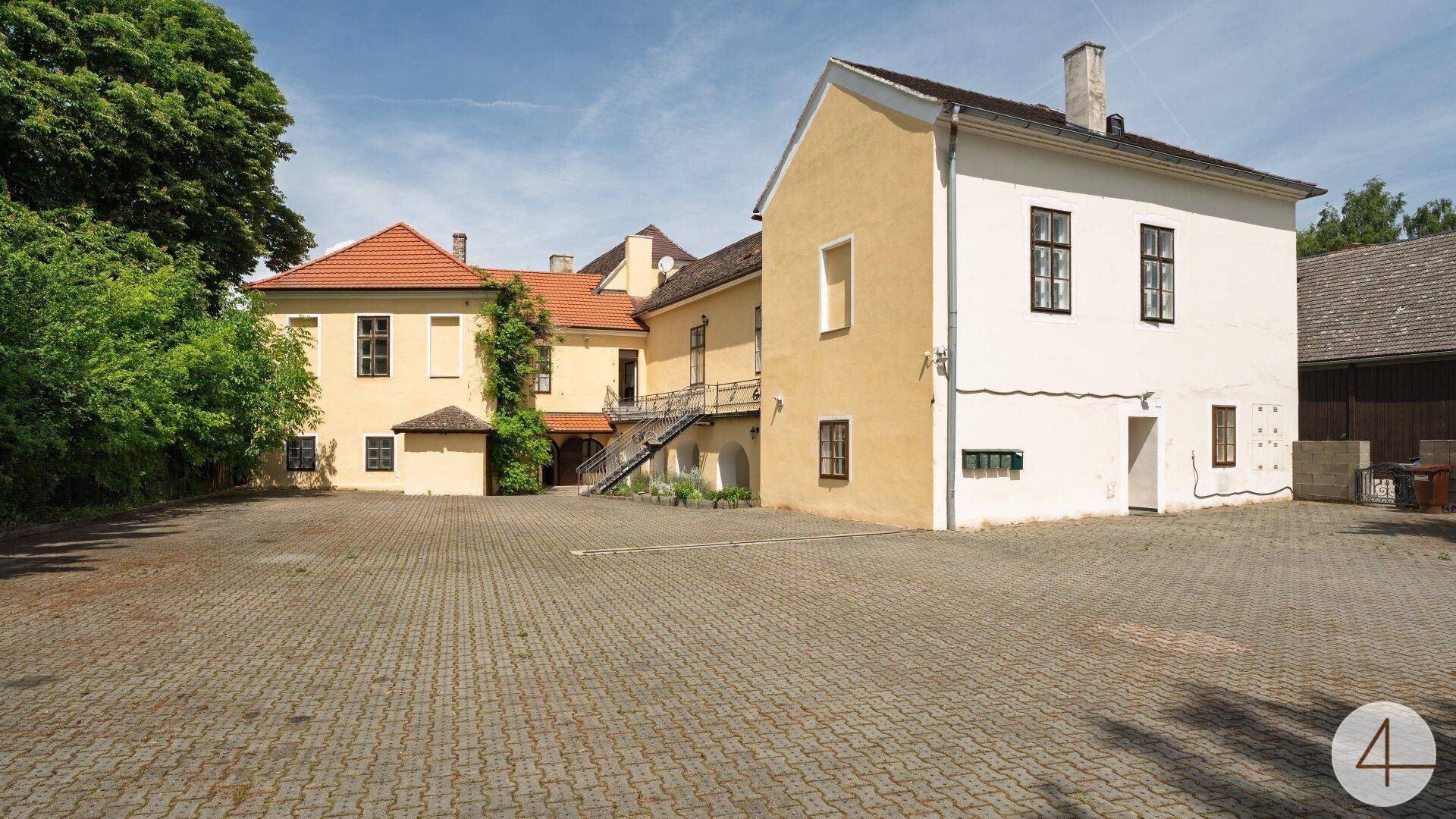 Historisches Gebäudeensemble mit gepflastertem Vorplatz und traditioneller Architektur unter blauem Himmel.