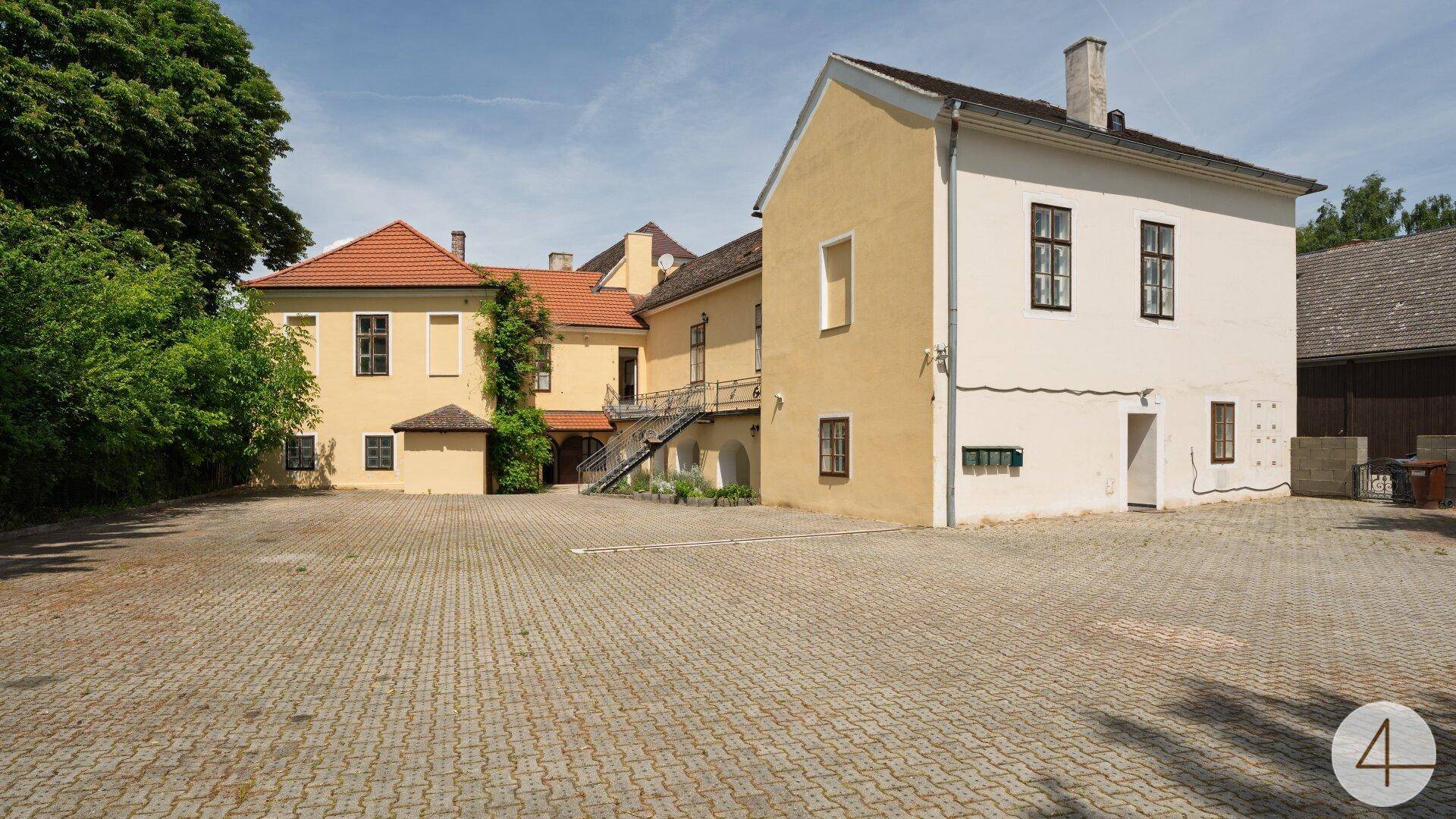 Historisches Gebäudeensemble mit gepflastertem Vorplatz und traditioneller Architektur unter blauem Himmel.