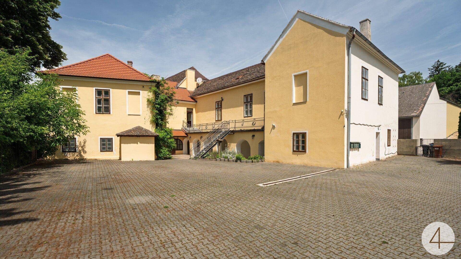Historisches Gebäudeensemble mit gepflastertem Vorplatz und traditioneller Architektur unter blauem Himmel.