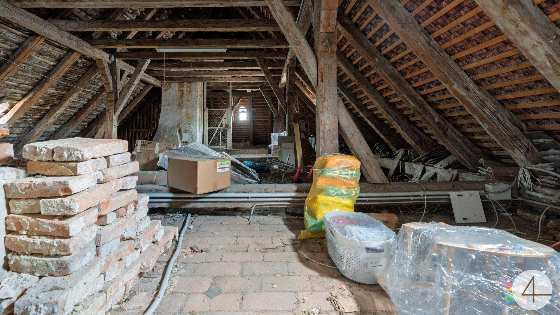 Geräumiger Dachboden mit sichtbaren Holzbalken und Ziegeln, bereit für den Ausbau.