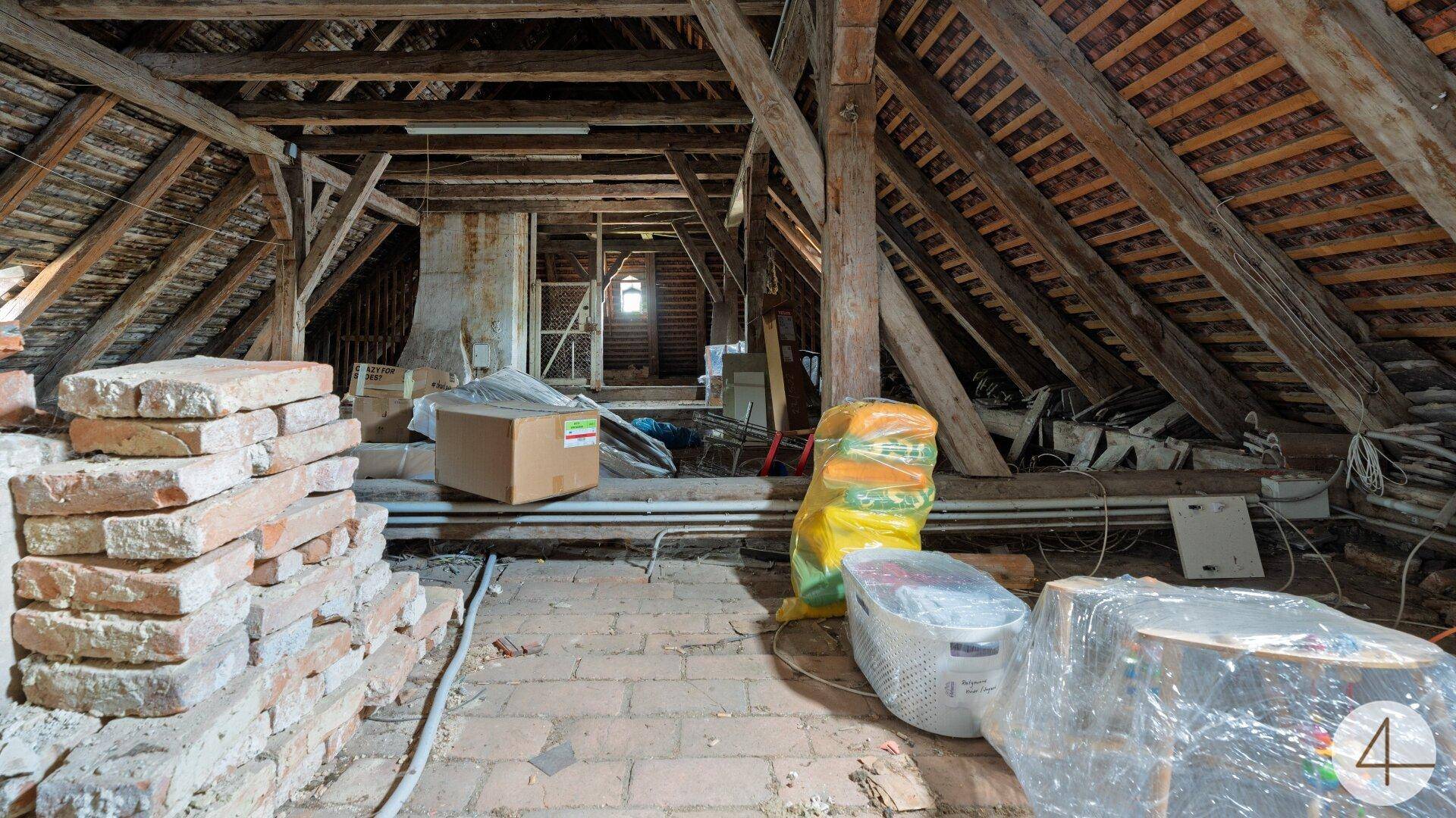 Geräumiger Dachboden mit sichtbaren Holzbalken und Ziegeln, bereit für den Ausbau.