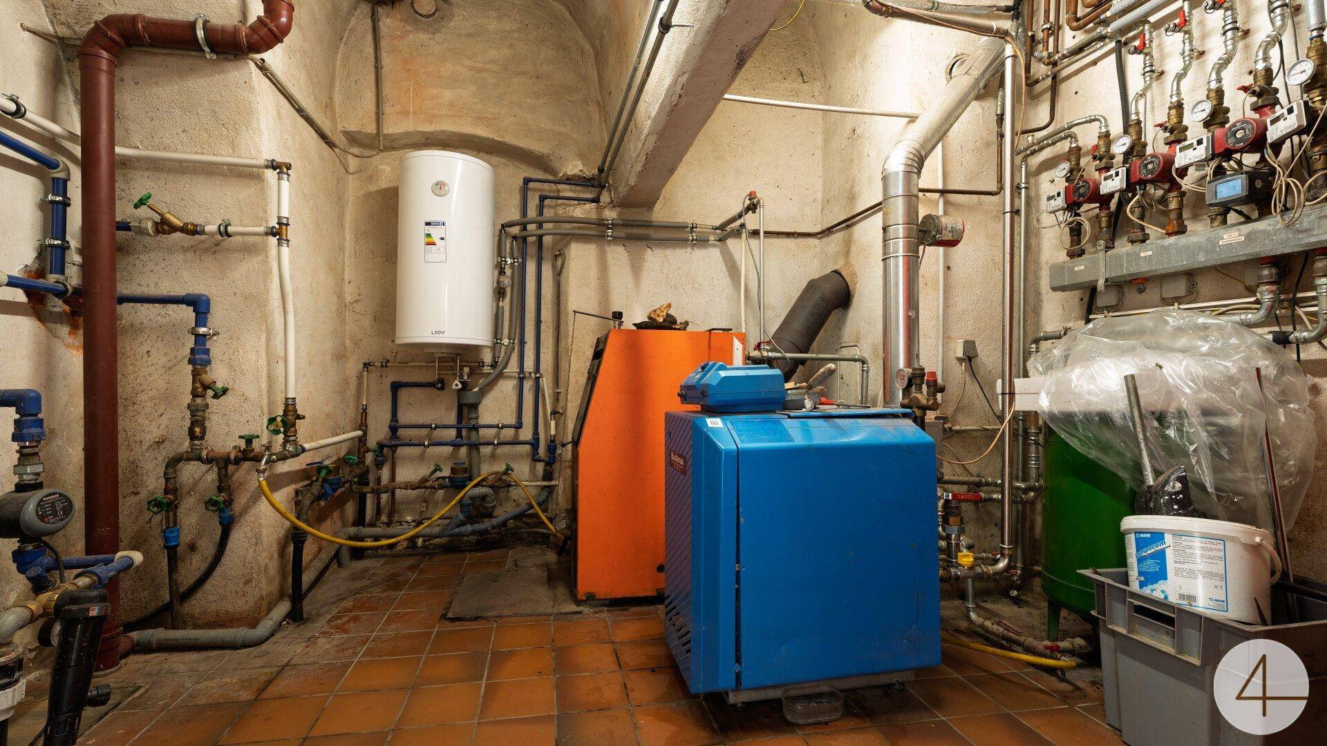 Heizungsraum mit verschiedenen Rohren, Kesseln und einem Warmwasserspeicher.