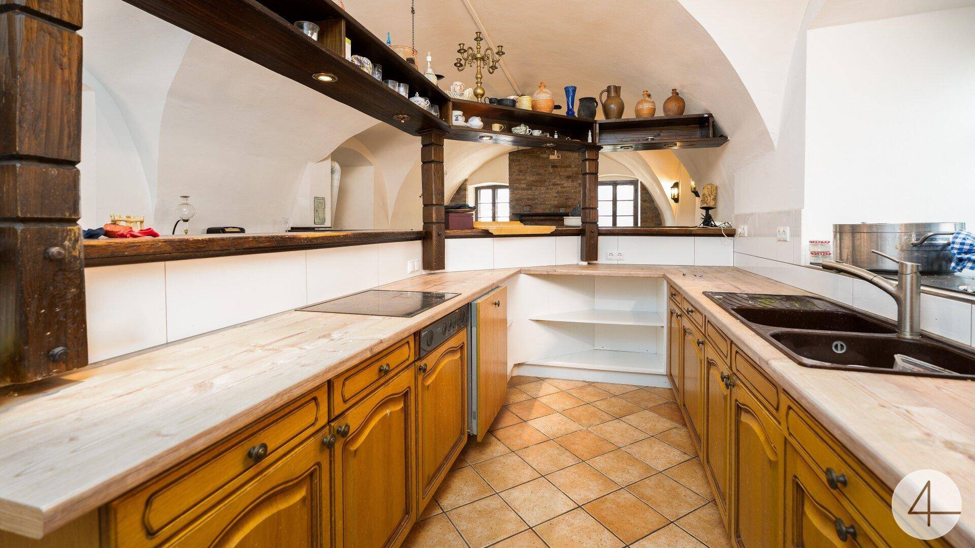 Traditionelle Küche mit Holzschränken, Fliesenboden und Arbeitsplatten, unter einem Gewölbedach.