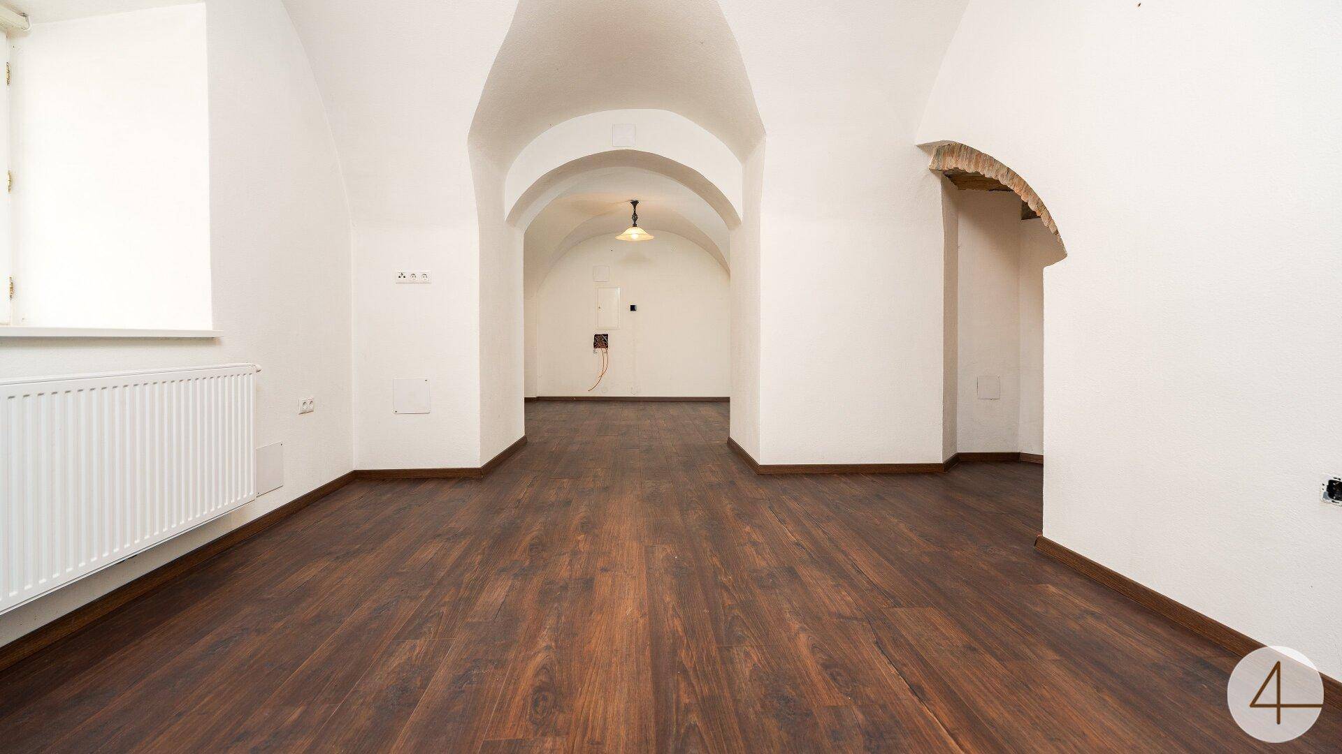 Geräumiger Raum mit dunklem Laminatboden und weiß getünchten Gewölbedecken, bereit zur individuellen Gestaltung.