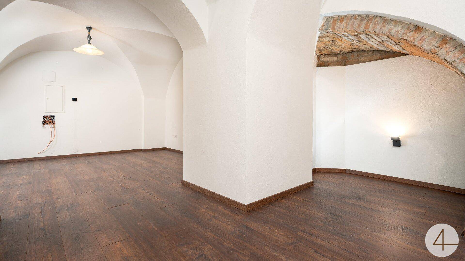 Gewölbekeller mit dunklem Laminatboden und freiliegenden Ziegelbögen, bereit zur Nutzung.