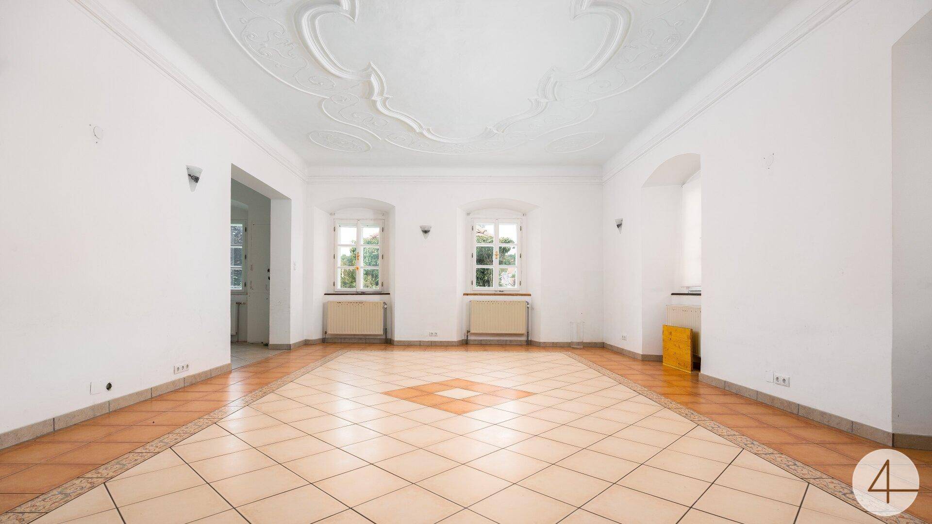 Geräumiges Wohnzimmer mit hohen Decken, Stuckverzierung und Terrakotta-Fliesenboden in einem historischen Gebäude.
