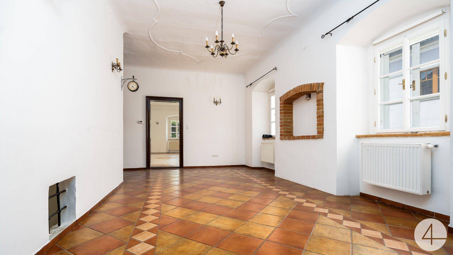 Helles Wohnzimmer mit Stuckdecke, Terrakotta-Fliesenboden und einem dekorativen Ziegelbogen.