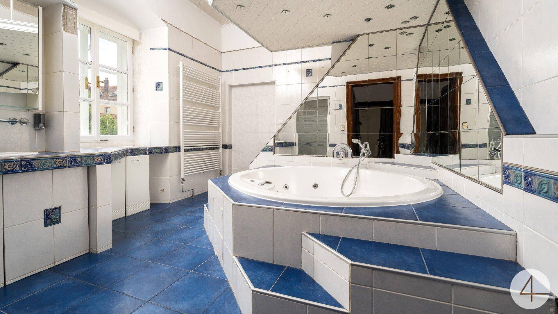 Geräumiges Badezimmer mit blauen Fliesen, Whirlpool-Badewanne und Spiegelflächen, im Stil der 80er Jahre.