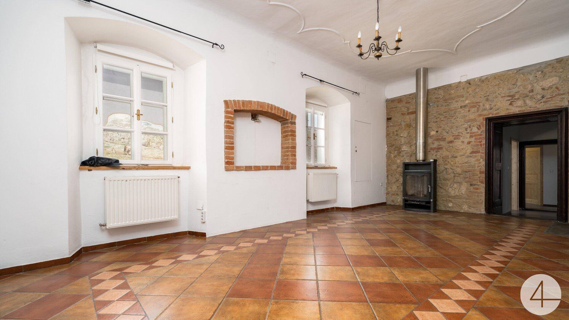 Geräumiges Wohnzimmer mit Terrakotta-Fliesenboden, Stuckdecke und einem modernen Kaminofen.