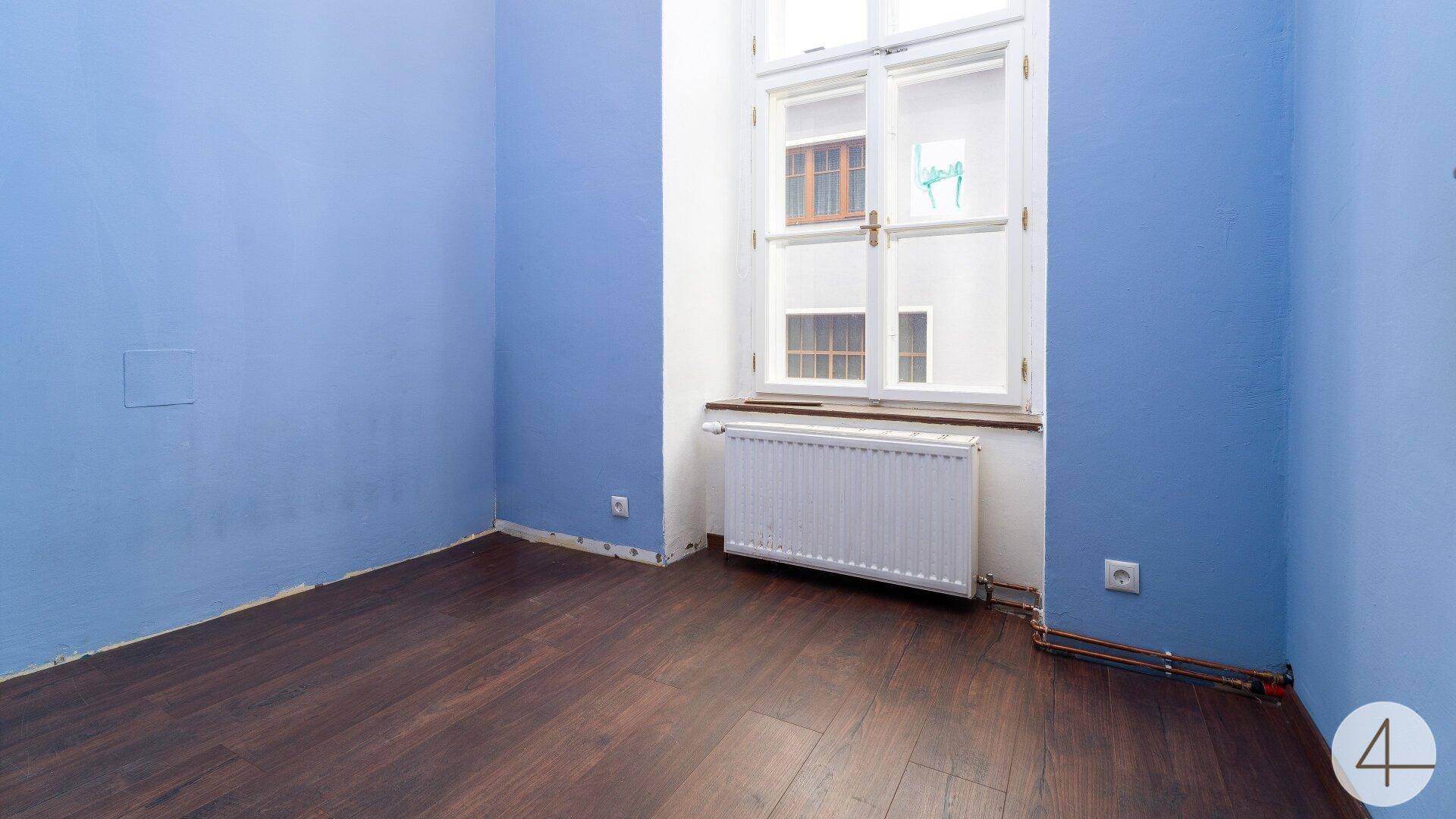 Schlafzimmer mit blau gestrichenen Wänden, dunklem Laminatboden und einem großen Fenster.