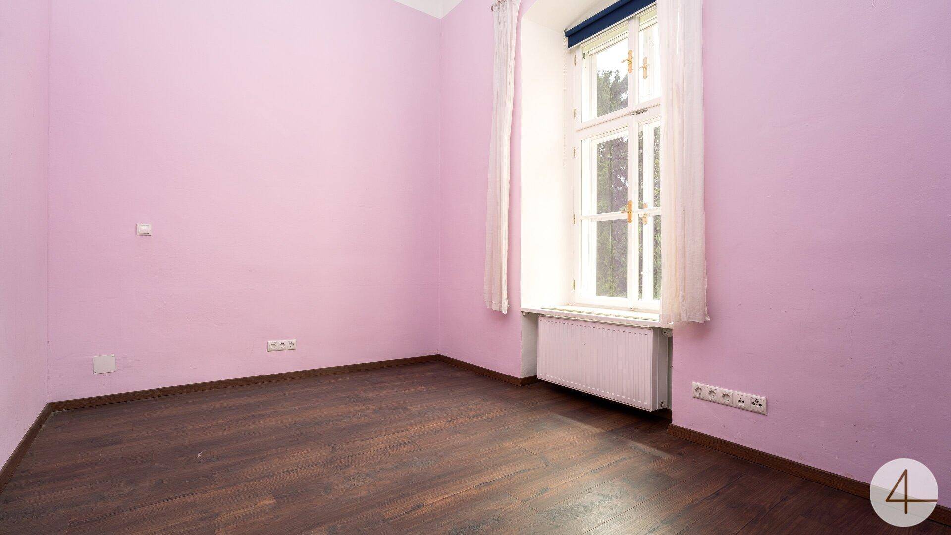 Schlafzimmer mit lila gestrichenen Wänden, dunklem Laminatboden und einem großen Fenster.