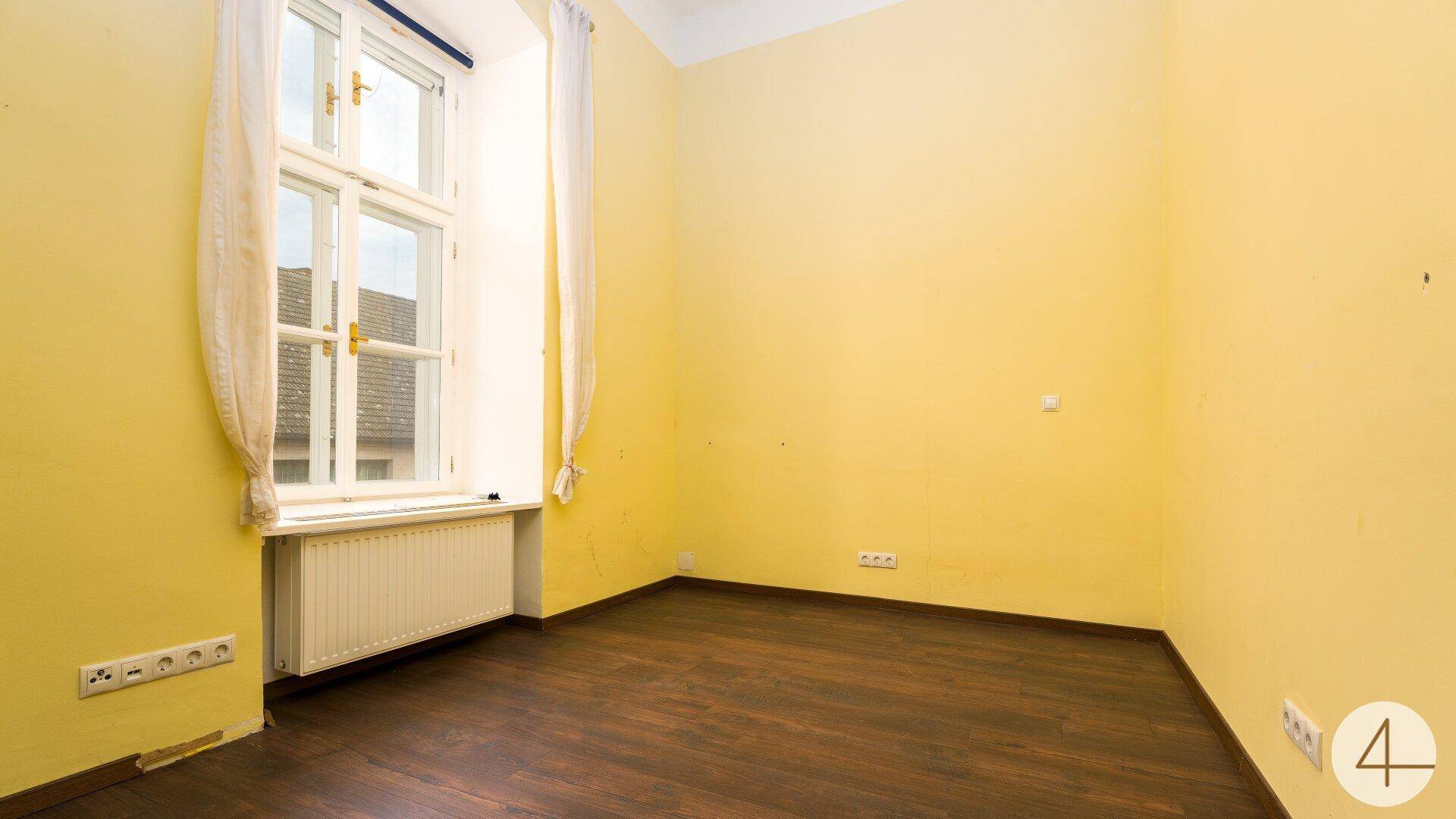 Schlafzimmer mit gelb gestrichenen Wänden, dunklem Laminatboden und einem großen Fenster.