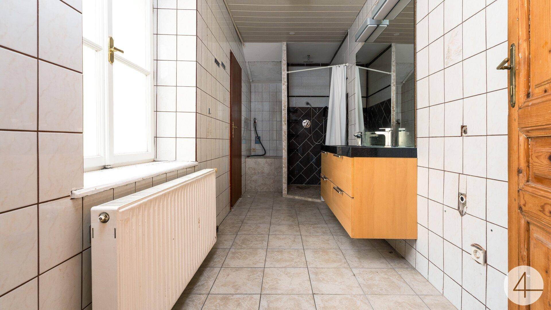 Gefliestes Badezimmer mit Fenster, Duschbereich und einem schwebenden Holzwaschtisch.