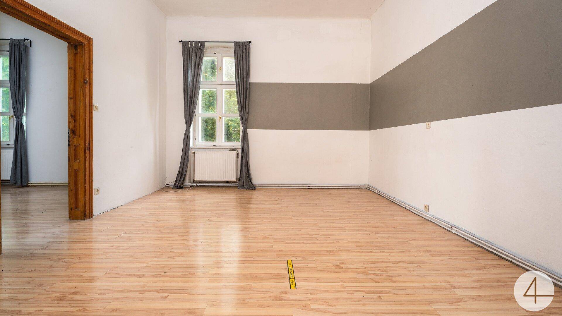Helles Wohnzimmer mit hellem Laminatboden und einer grauen Akzentwand, bereit zur Einrichtung.