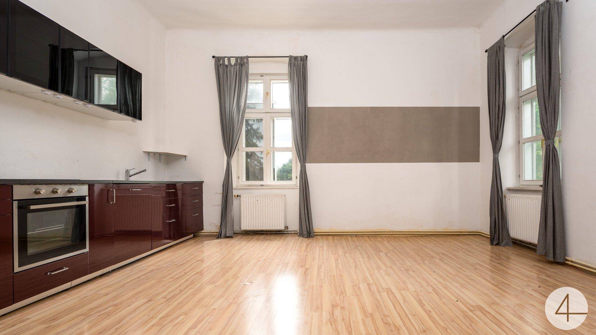 Moderne Küche mit glänzenden roten Unterschränken, integriertem Backofen und hellem Laminatboden.