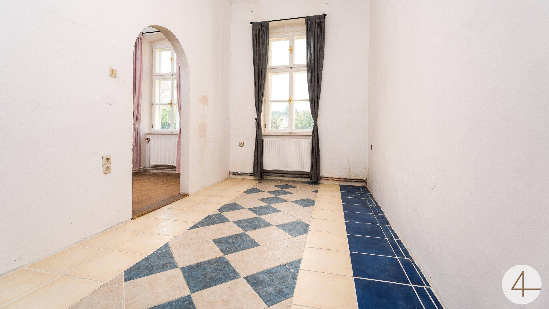 Geräumiger Raum mit gemusterten Fliesen und einem Durchgang zu einem weiteren Zimmer.