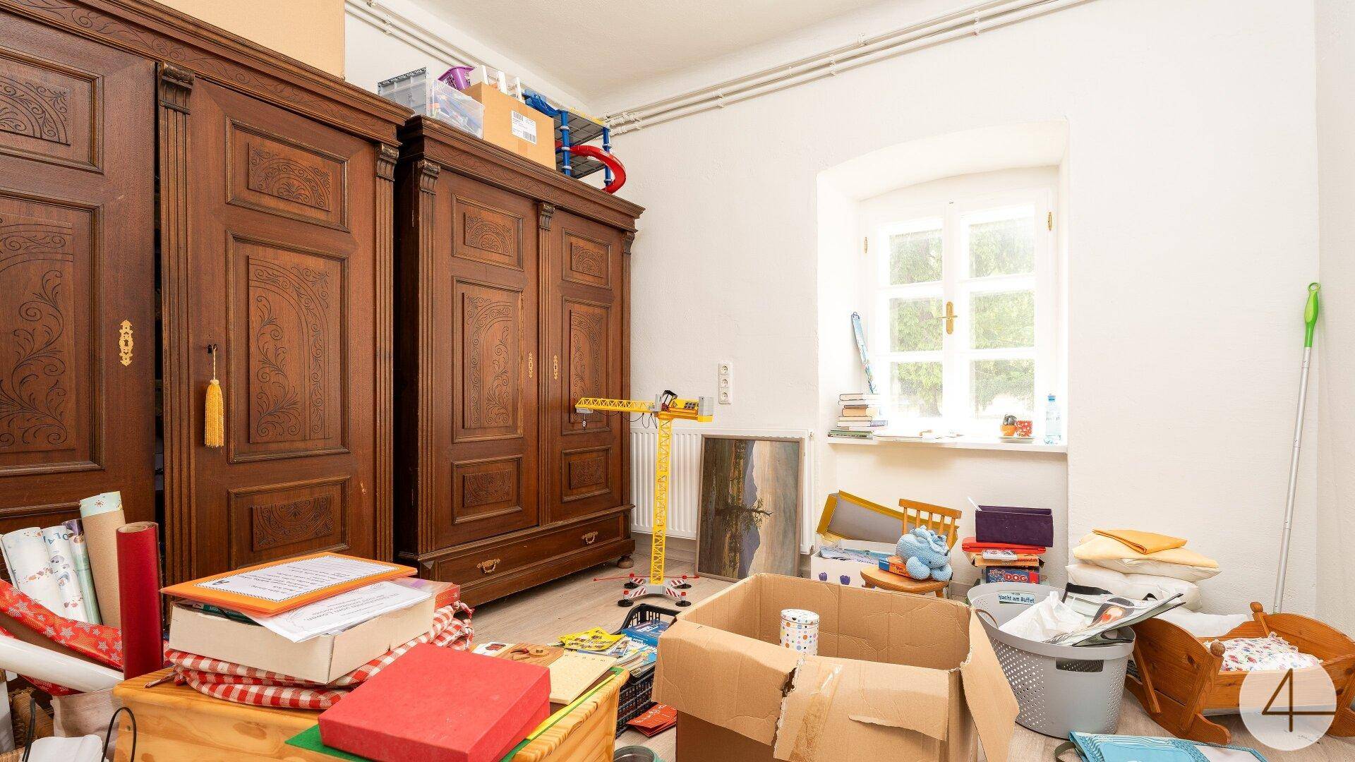 Unaufgeräumter Raum mit alten Holzschränken und einem Fenster, das auf einen Garten blickt.