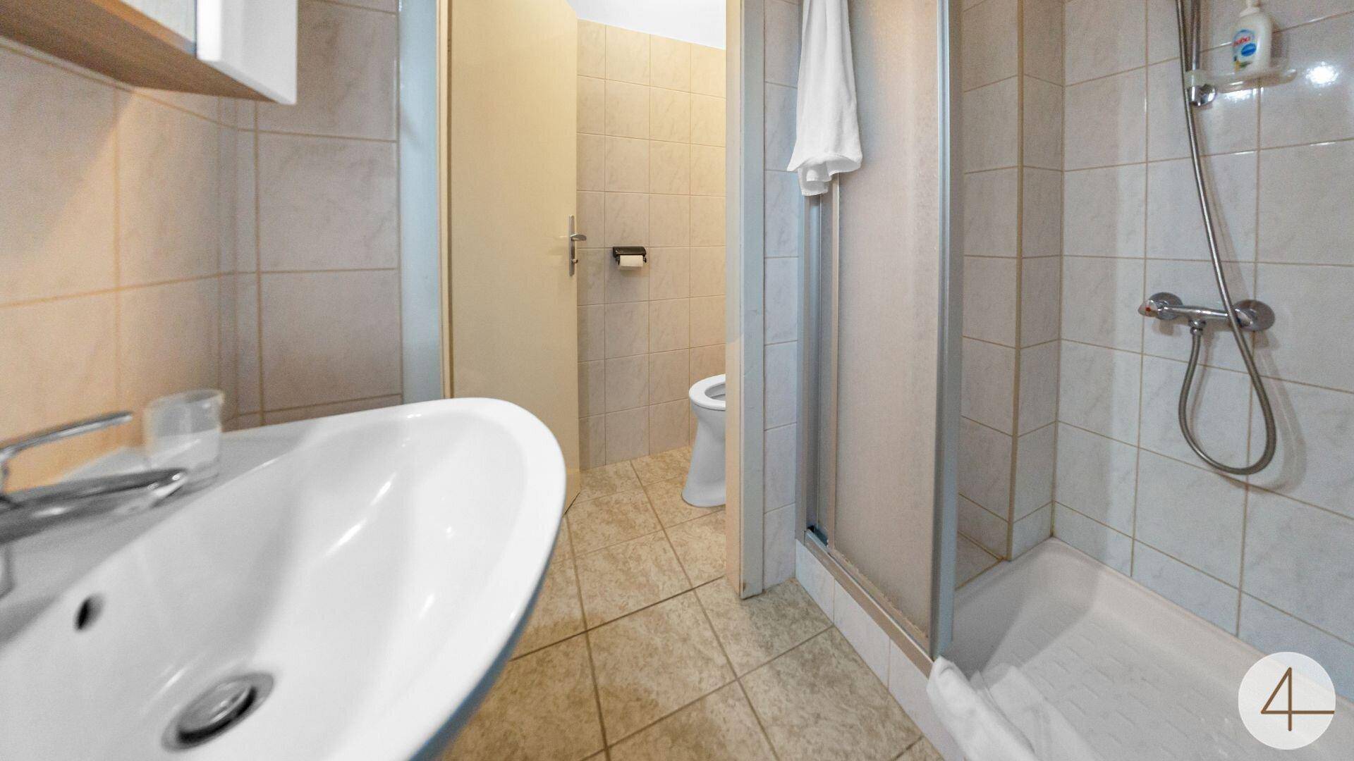 Kleines Badezimmer mit Duschkabine, Waschbecken und hellen Fliesen an Wänden und Boden.