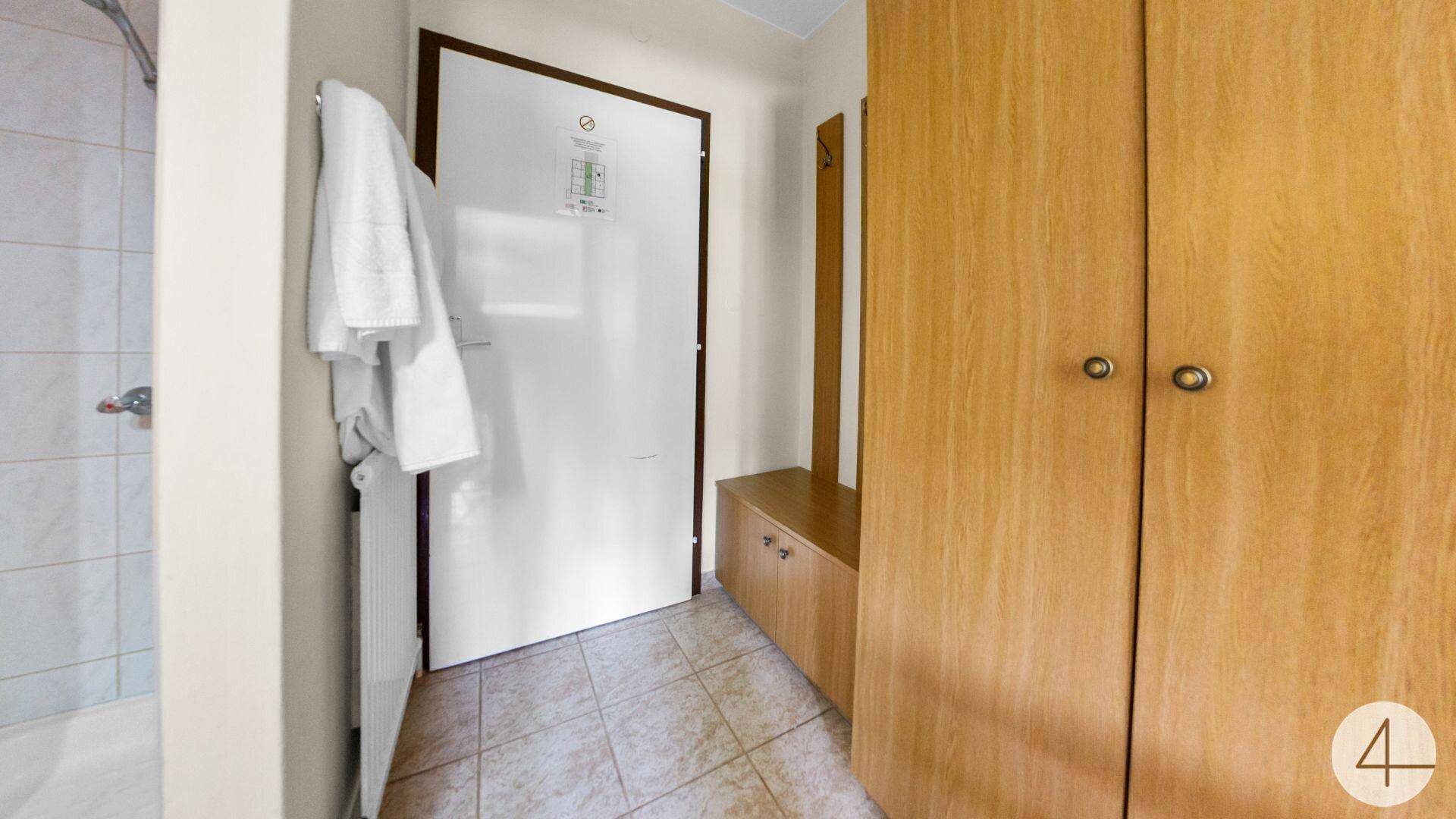 Flur mit Holzkleiderschrank und Fliesenboden, der zu einem Badezimmer führt.