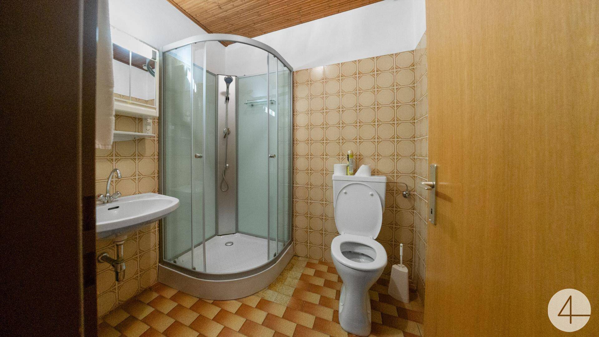 Badezimmer mit Duschkabine, WC und Waschbecken, gefliest in warmen Terrakotta-Tönen.