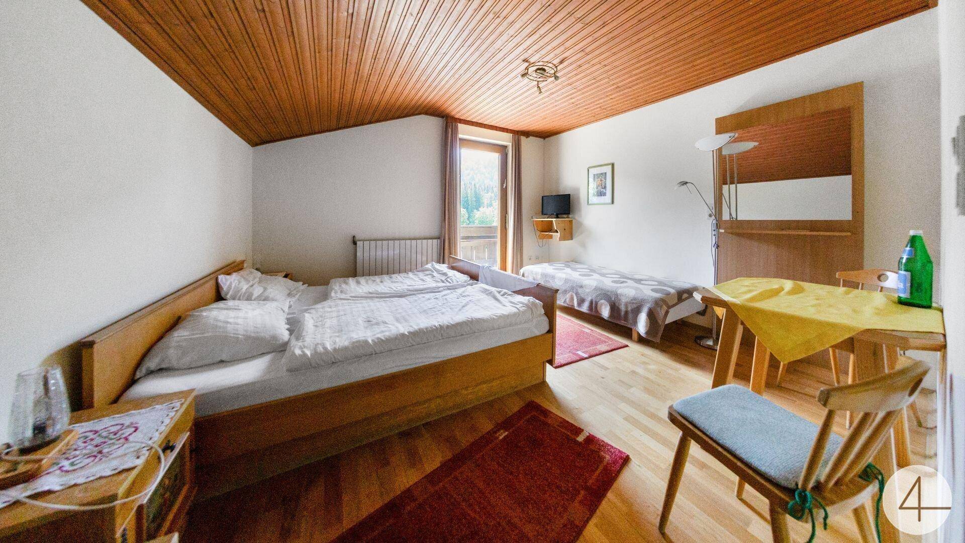 Schlafzimmer mit Doppelbett, Holzboden und Holzdecke, Zugang zu einem Balkon.