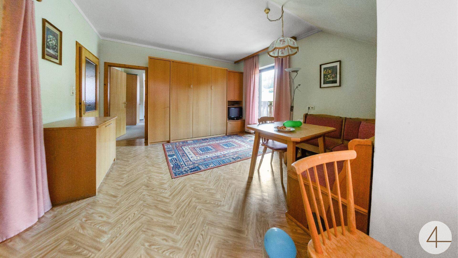 Wohnzimmer mit Holzboden, Esstisch und großem Kleiderschrank, Fenster mit Blick ins Grüne.
