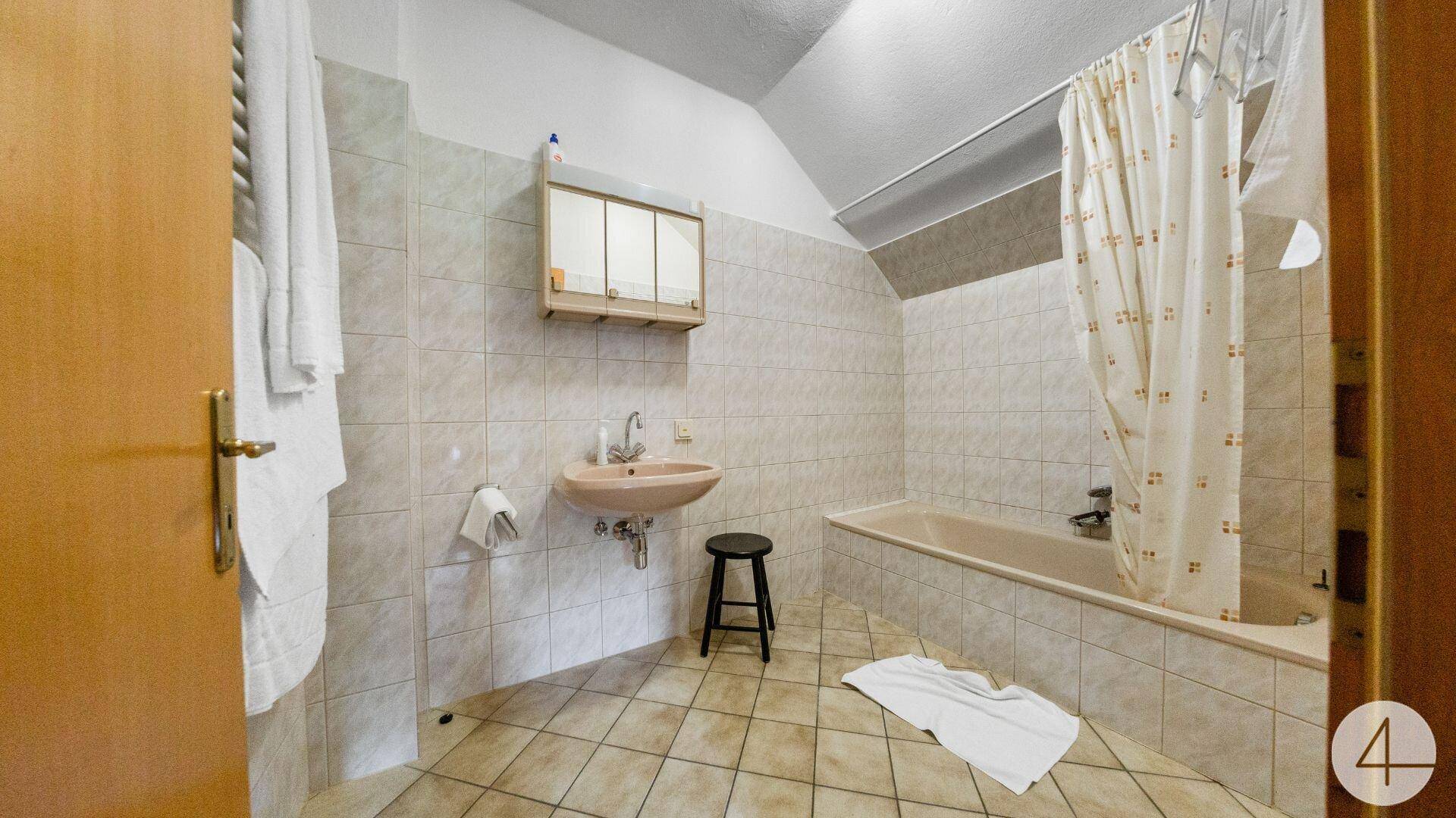 Badezimmer mit Badewanne, Waschbecken und Fliesen an Wänden und Boden, mit Dachschräge.