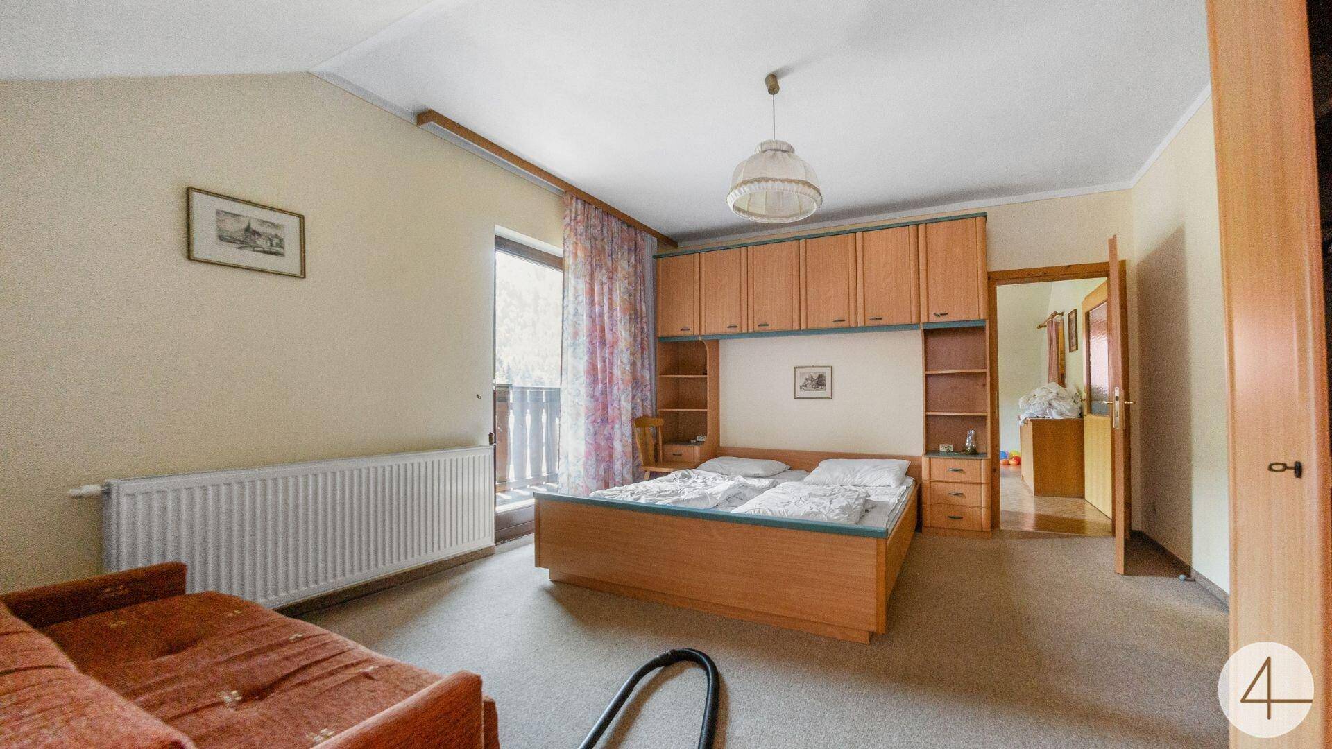 Schlafzimmer mit Doppelbett, Teppichboden und Einbauschränken, Zugang zu einem Balkon.