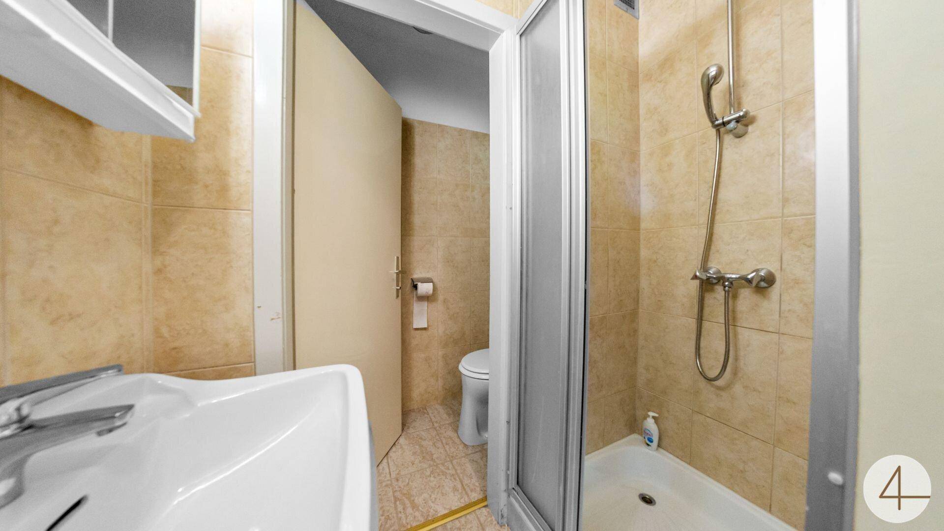 Badezimmer mit Duschkabine, Waschbecken und WC, gefliest in warmen Beigetönen.