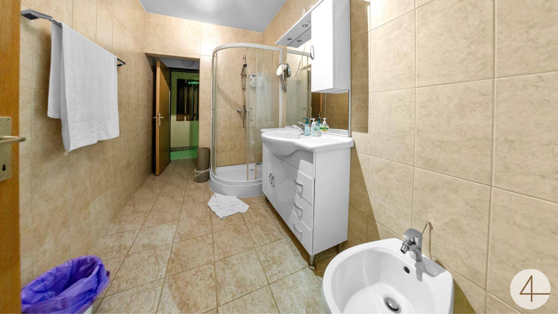 Badezimmer mit Duschkabine, Waschbecken und Bidet, komplett gefliest in Beige.