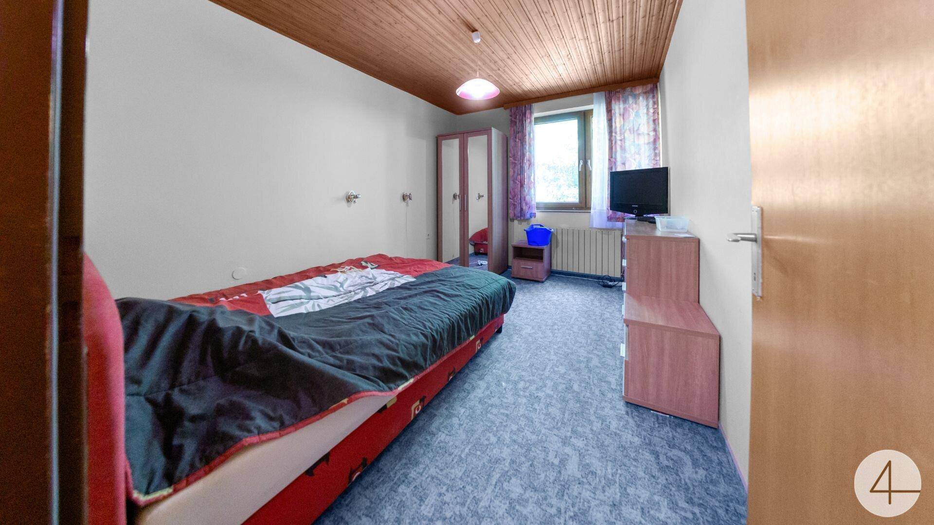 Schlafzimmer mit Einzelbett, Teppichboden und Holzdecke, ausgestattet mit TV und Schrank.