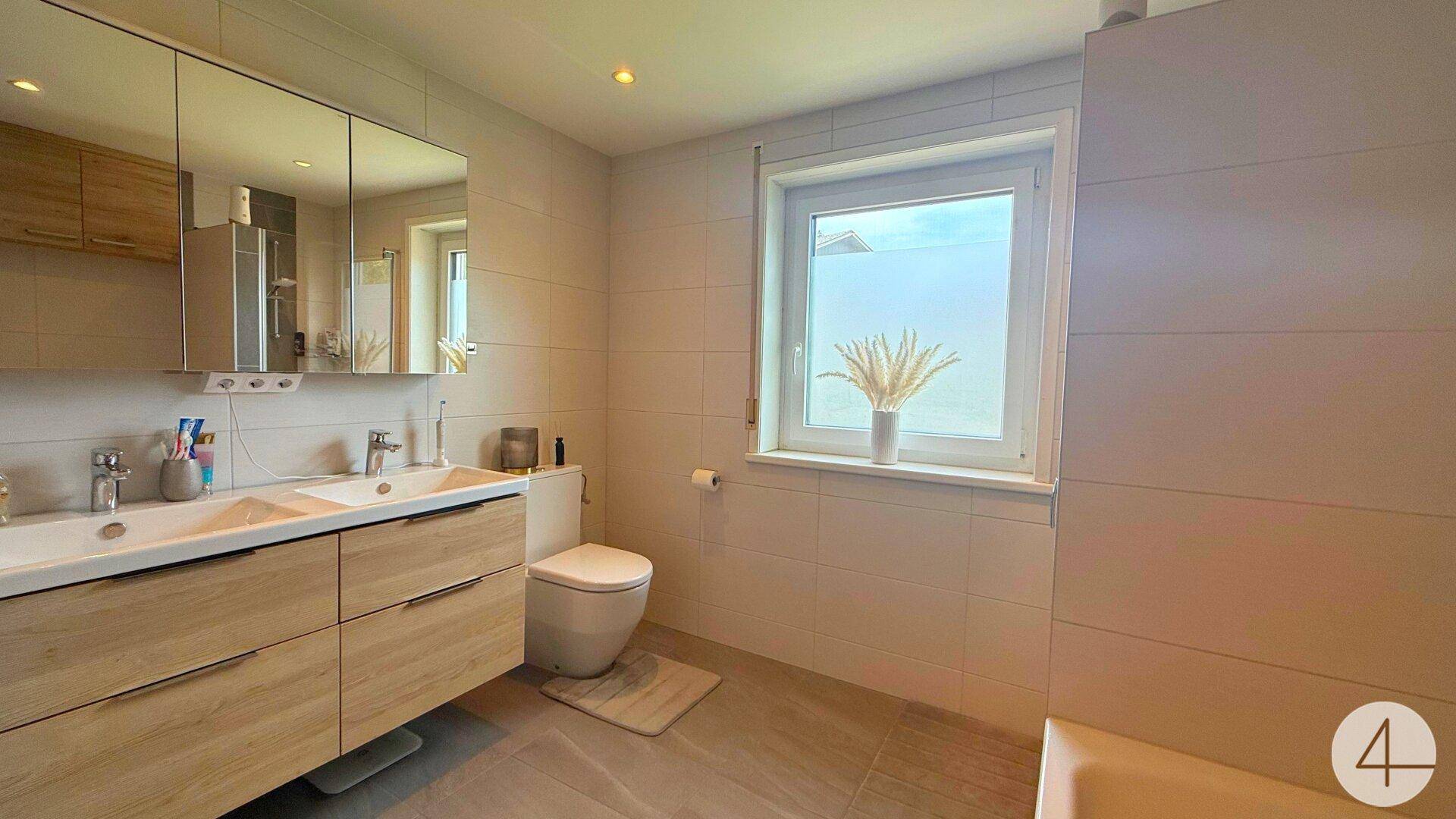 Helles Badezimmer mit Doppelwaschbecken, Spiegelschrank und Fenster für Tageslicht.