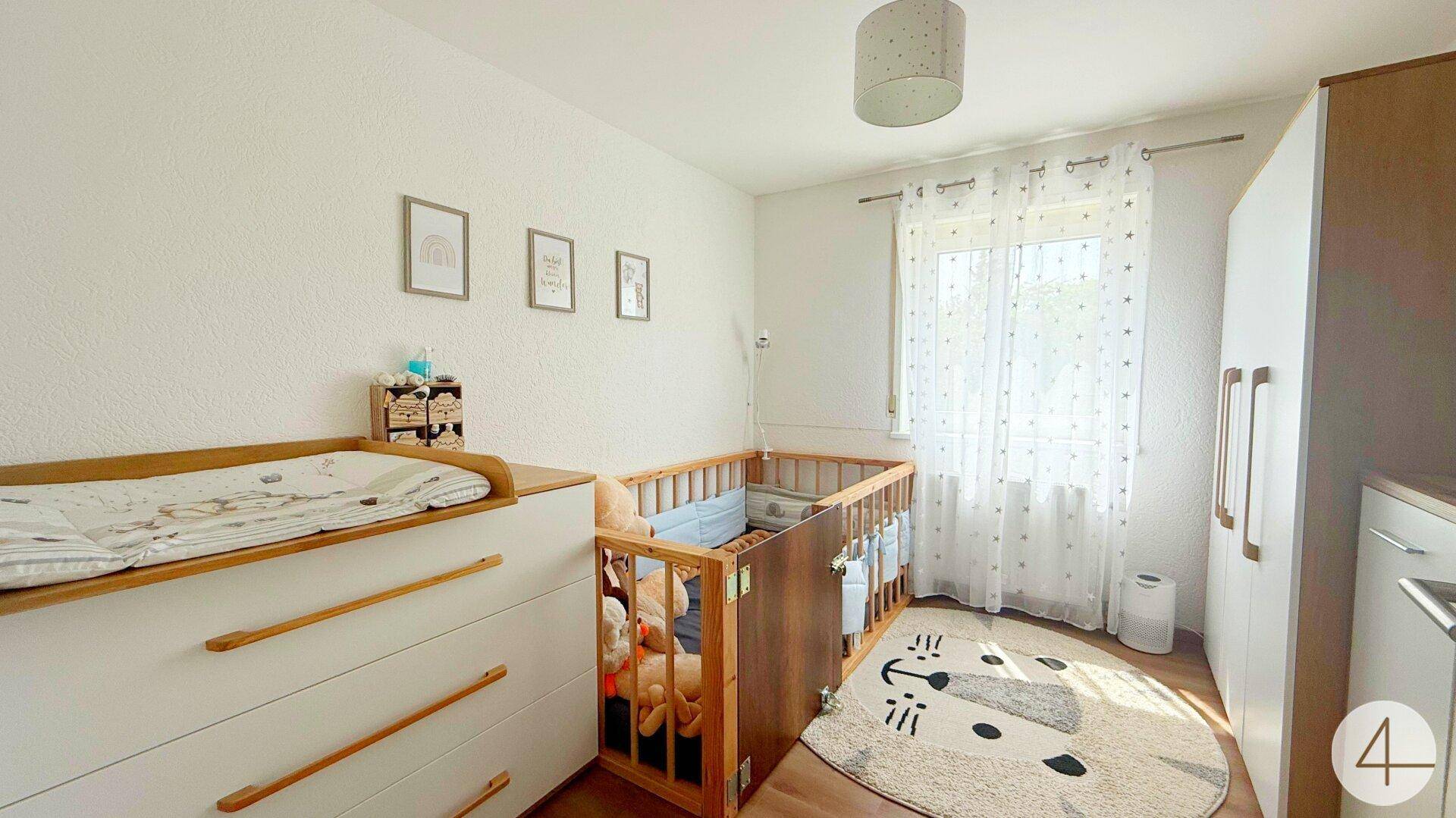 Helles Kinderzimmer mit Babybett, Wickelkommode und einem freundlichen Teppich.