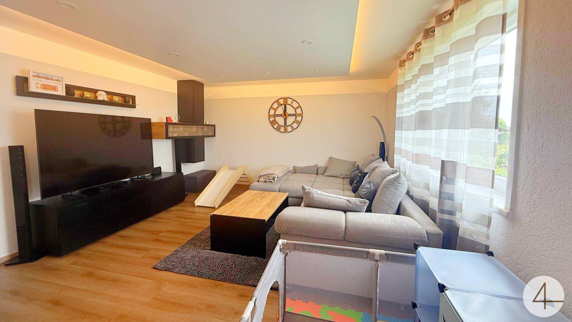 Gemütliches Wohnzimmer mit großem Ecksofa, Unterhaltungselektronik und Spielbereich für Kinder.