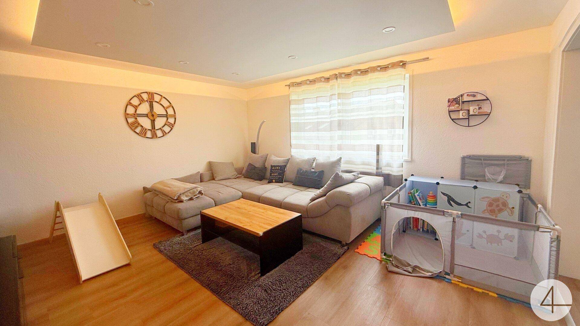Helles Wohnzimmer mit großem Ecksofa, Couchtisch und einem Spielbereich für Kleinkinder.
