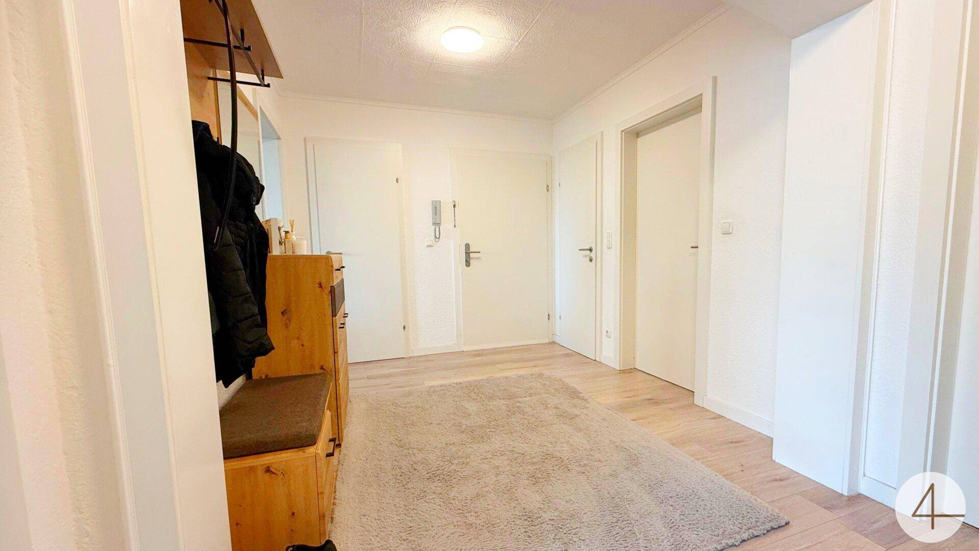 Heller Eingangsbereich mit Garderobe, Schuhschrank und Teppich auf Laminatboden.