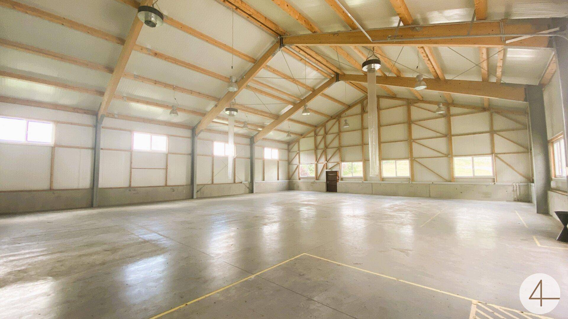 Große, leere Lagerhalle mit hohen Decken, sichtbaren Holzbalken und vielen Fenstern.