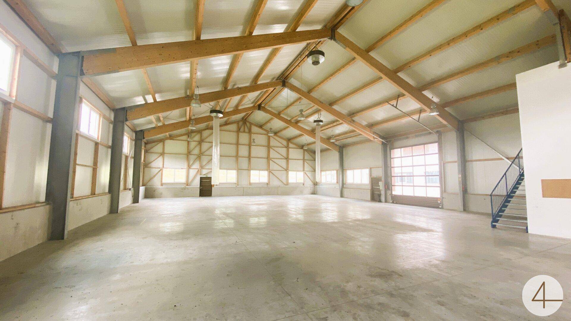 Geräumige Lagerhalle mit Betonboden, Holzdachkonstruktion und einer blauen Stahltreppe.