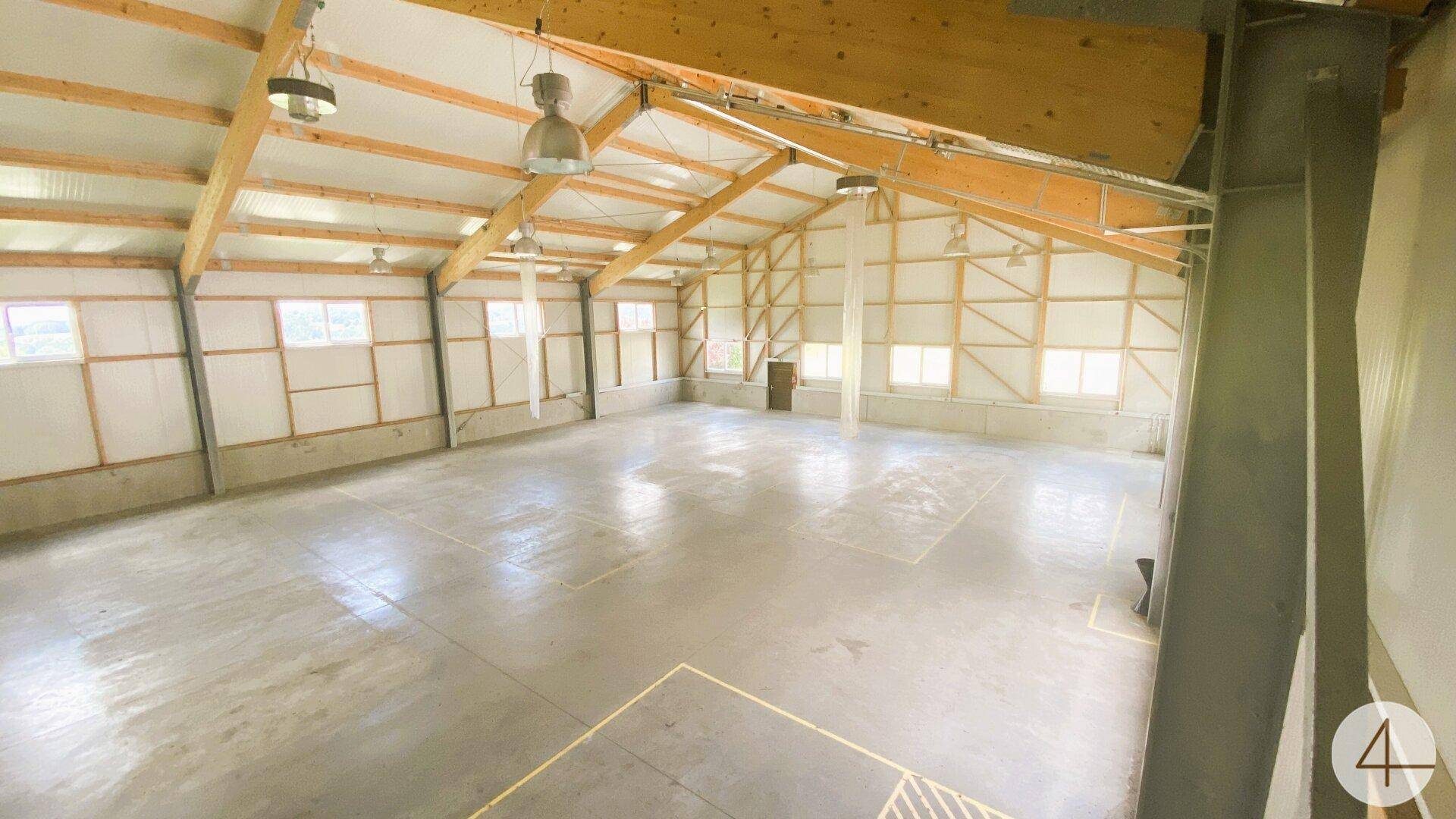Weitläufige Industriehalle mit hohen Decken, Holzbalken und hellen Wänden, ideal für Lagerung.