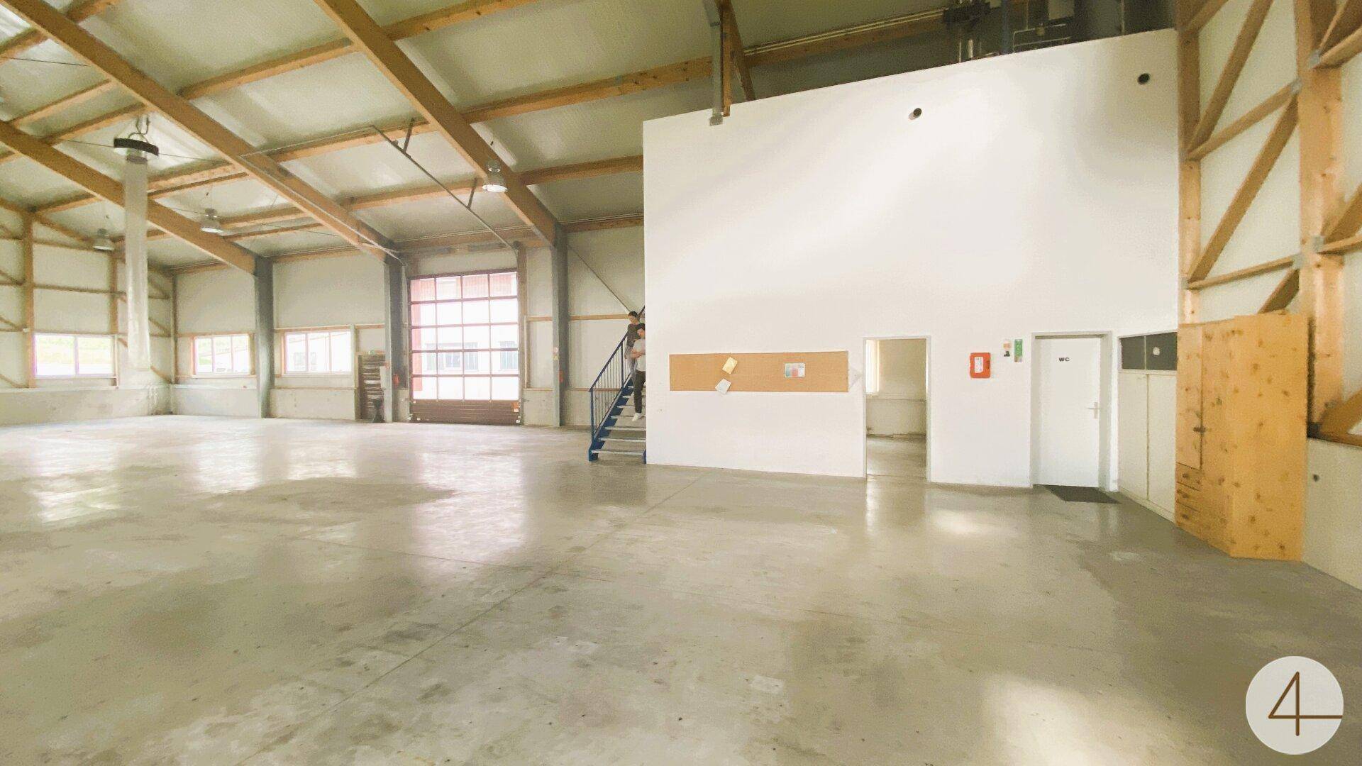 Große Lagerhalle mit Betonboden, Rolltor, blauer Treppe und Zugang zu weiteren Räumen.