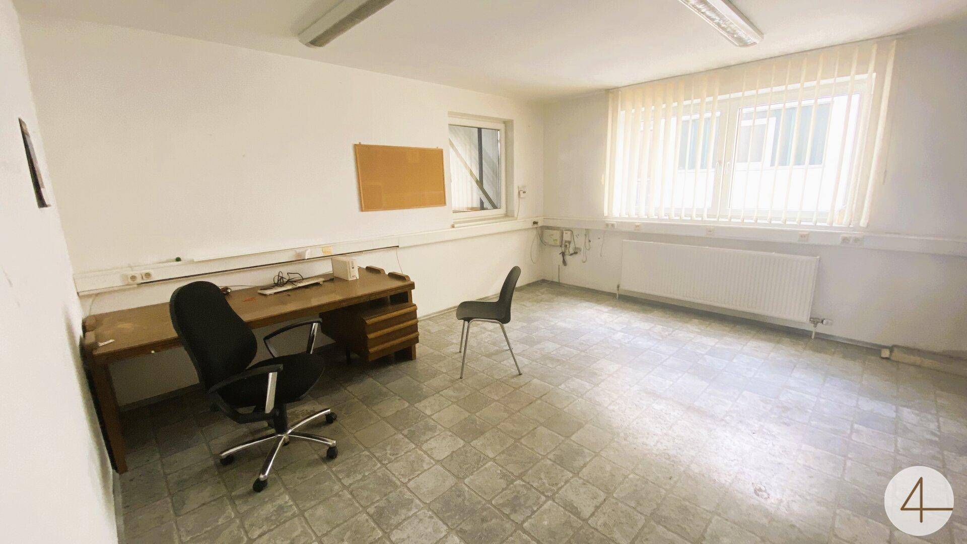 Büro mit Schreibtisch, Bürostuhl, Fenster mit Jalousien und gefliestem Boden.